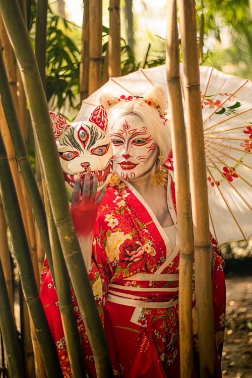 Free Artistic scene of a figure in a red kimono with mask in a bamboo forest. Stock Photo