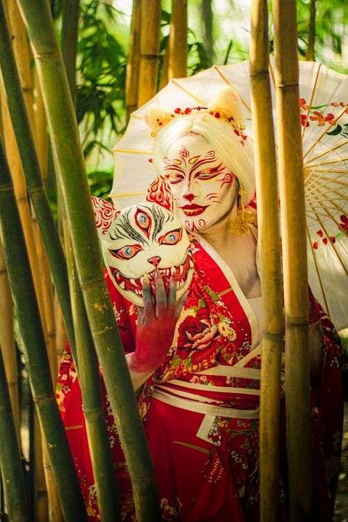 Free Geisha with artistic makeup and traditional kimono in bamboo grove holding a mask. Stock Photo
