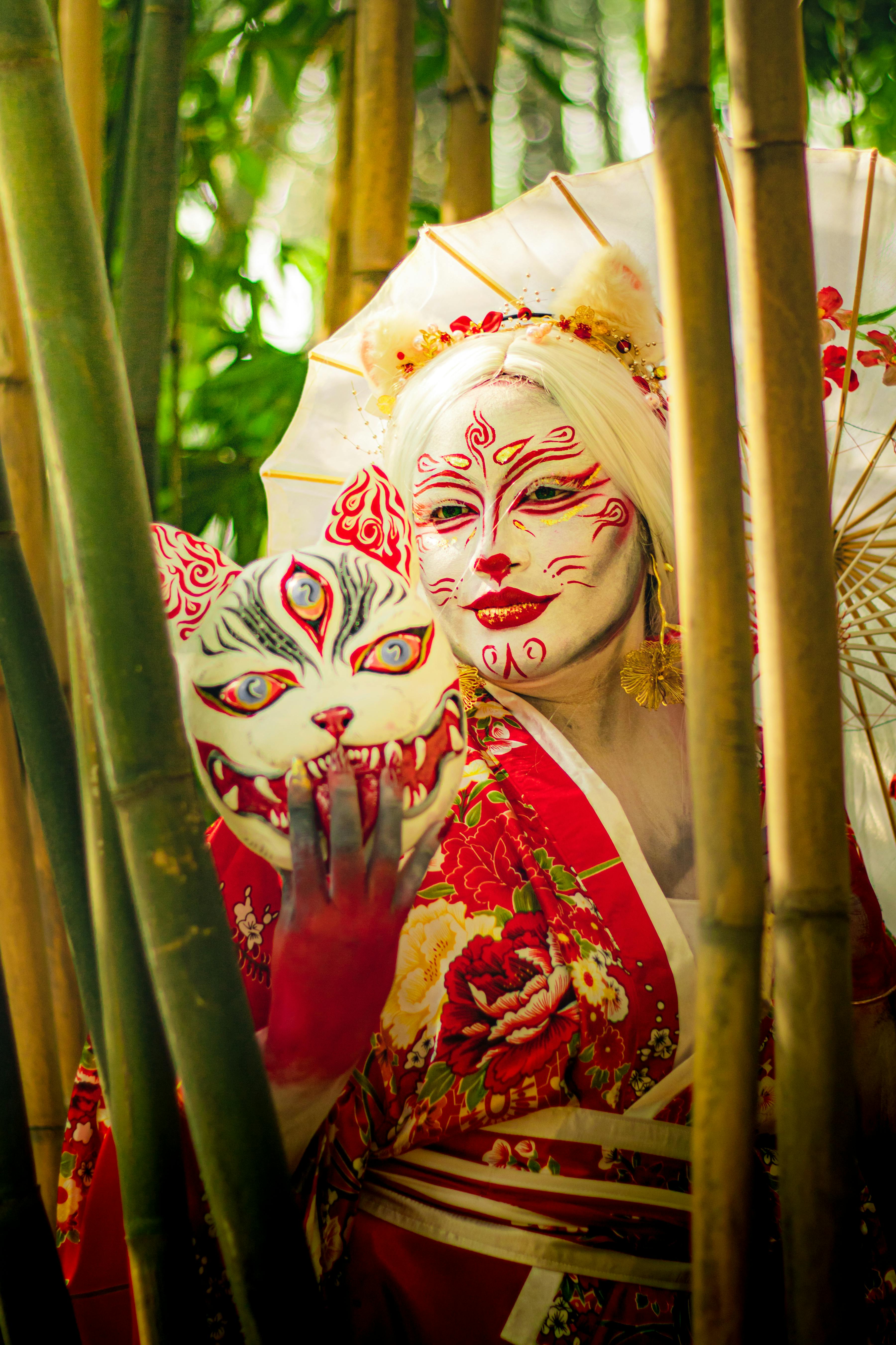 ฟรี ภาพวาดศิลปะของหญิงสาวในชุดกิโมโนสีแดง แต่งหน้าแบบละครเวที ถือหน้ากากจิ้งจอกอยู่ในป่าไผ่ คลังภาพถ่าย