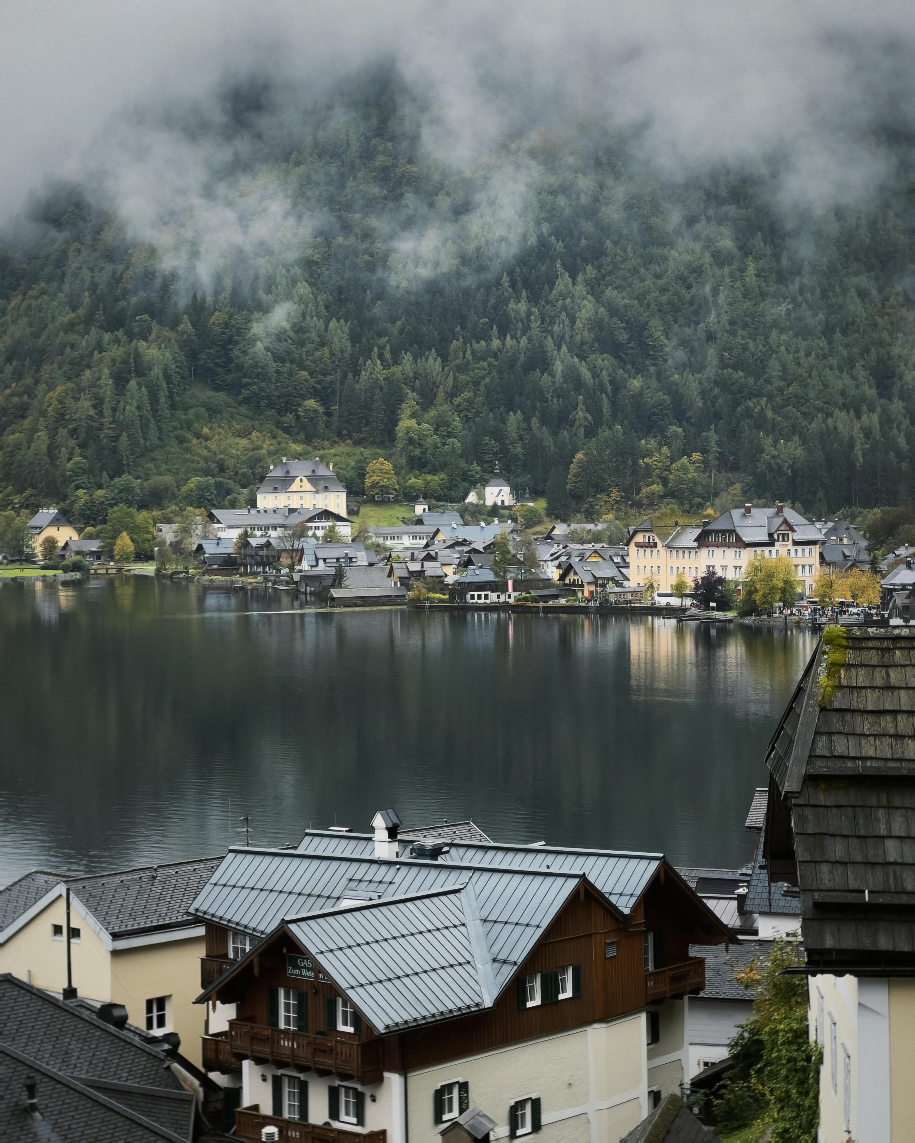bezplatná Úchvatný výhled na klidnou alpskou vesnici u klidného jezera pod zataženou oblohou, odrážející malebnou krajinu. Základová fotografie