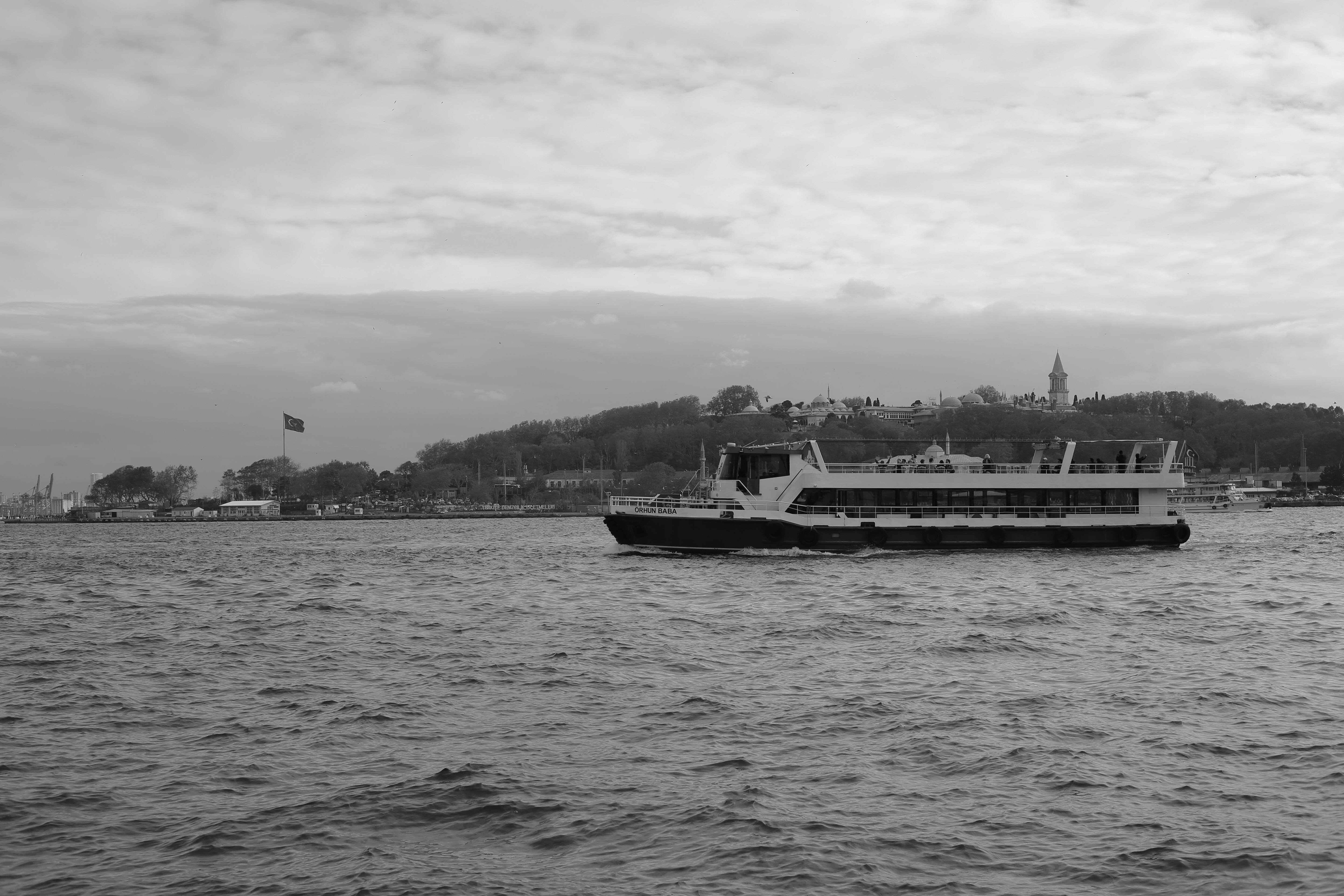 ฟรี ภาพขาวดำของเรือข้ามฟากในน่านน้ำชายฝั่งของอิสตันบูล โดยมีทิวทัศน์เมืองอยู่ไกลๆ คลังภาพถ่าย