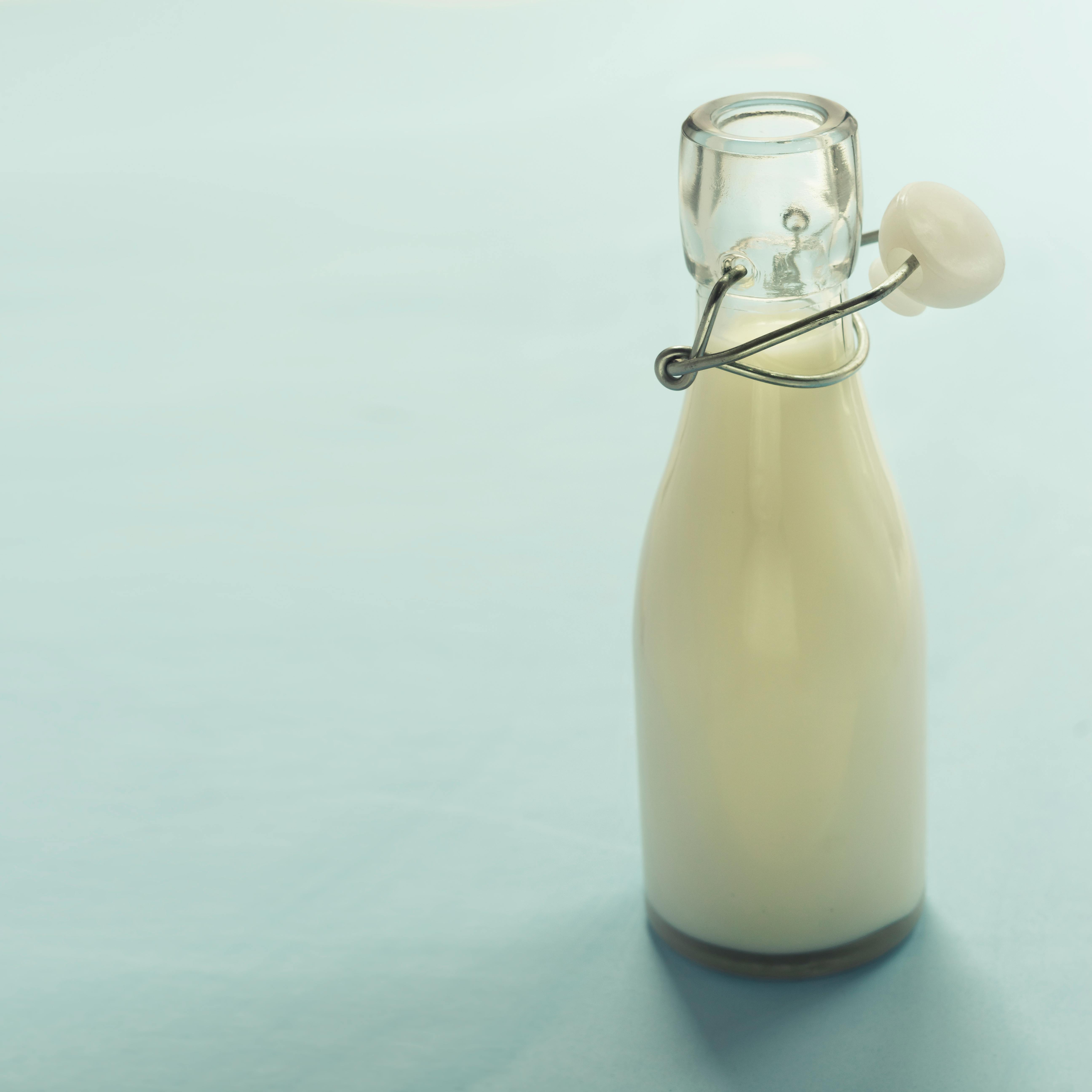 Free A minimalist image of a glass bottle filled with milk on a light blue background, offering ample copyspace. Stock Photo