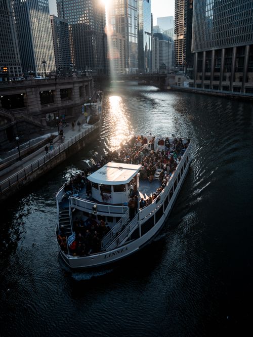 Free Tour boat filled with passengers travels along the Chicago River with a stunning cityscape view at sunset. Stock Photo