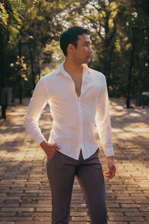 Free Young man in a white shirt walking confidently in a sunlit park, conveying serene confidence. Stock Photo