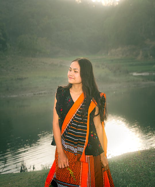 A serene woman in vibrant traditional clothing stands by a tranquil lake at sunset in Rangamati, Bangladesh.