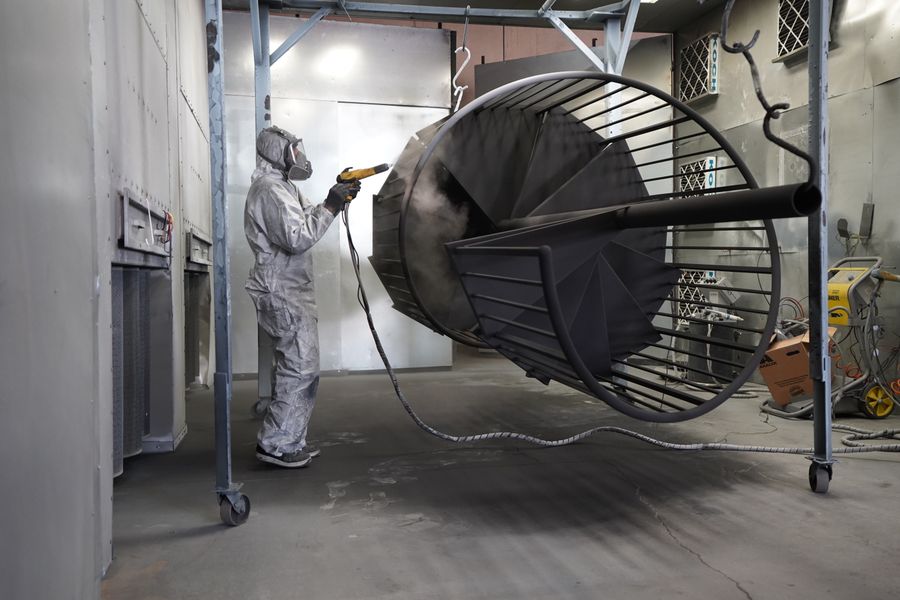 Worker spray coating a large metal structure in a controlled booth