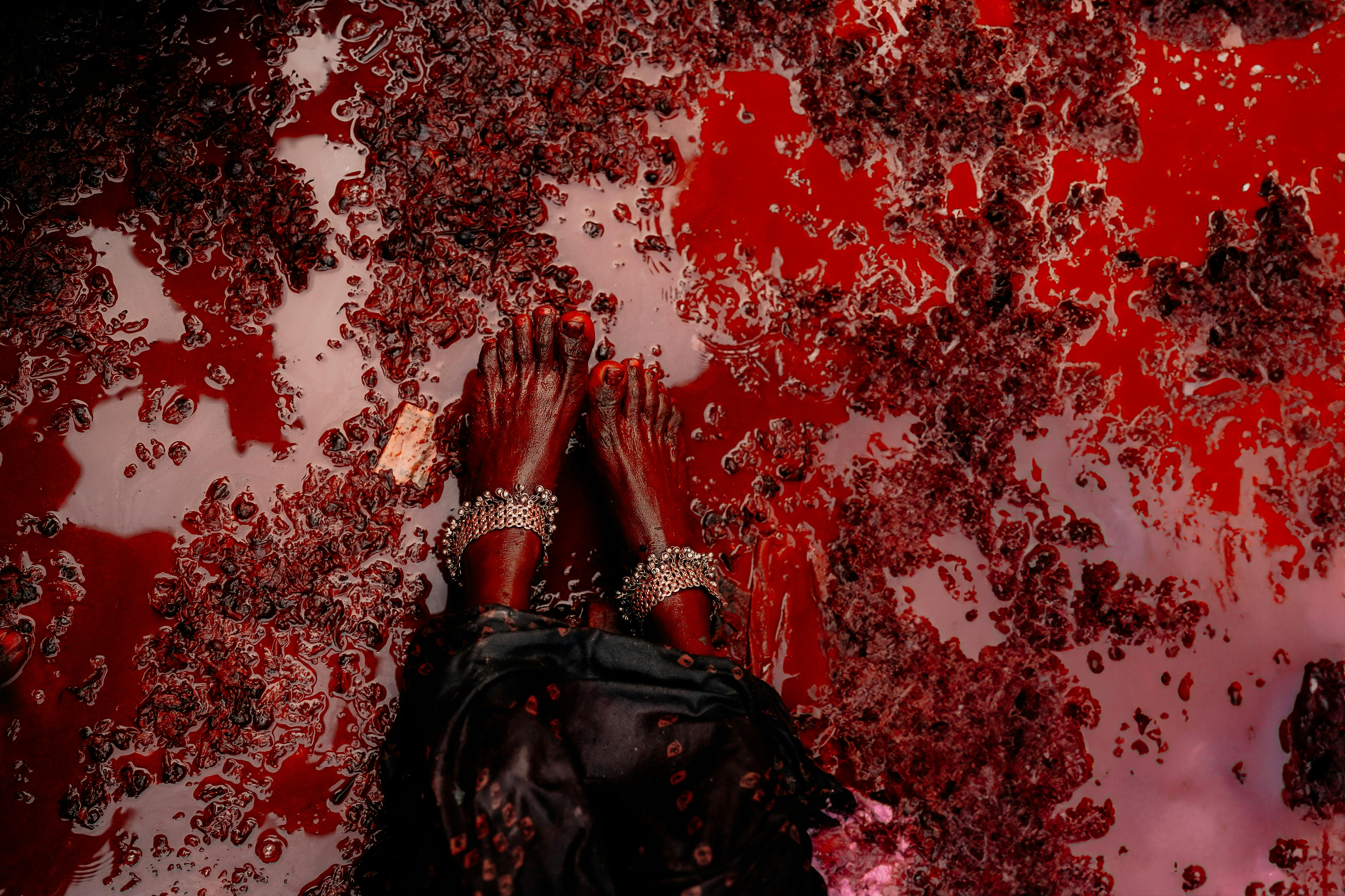 Ilmainen Taiteellinen lähikuva jaloista ja nilkkarenkaista, jotka ovat upotettuina kirkkaanpunaiseen nesteeseen. Kuvapankkikuva