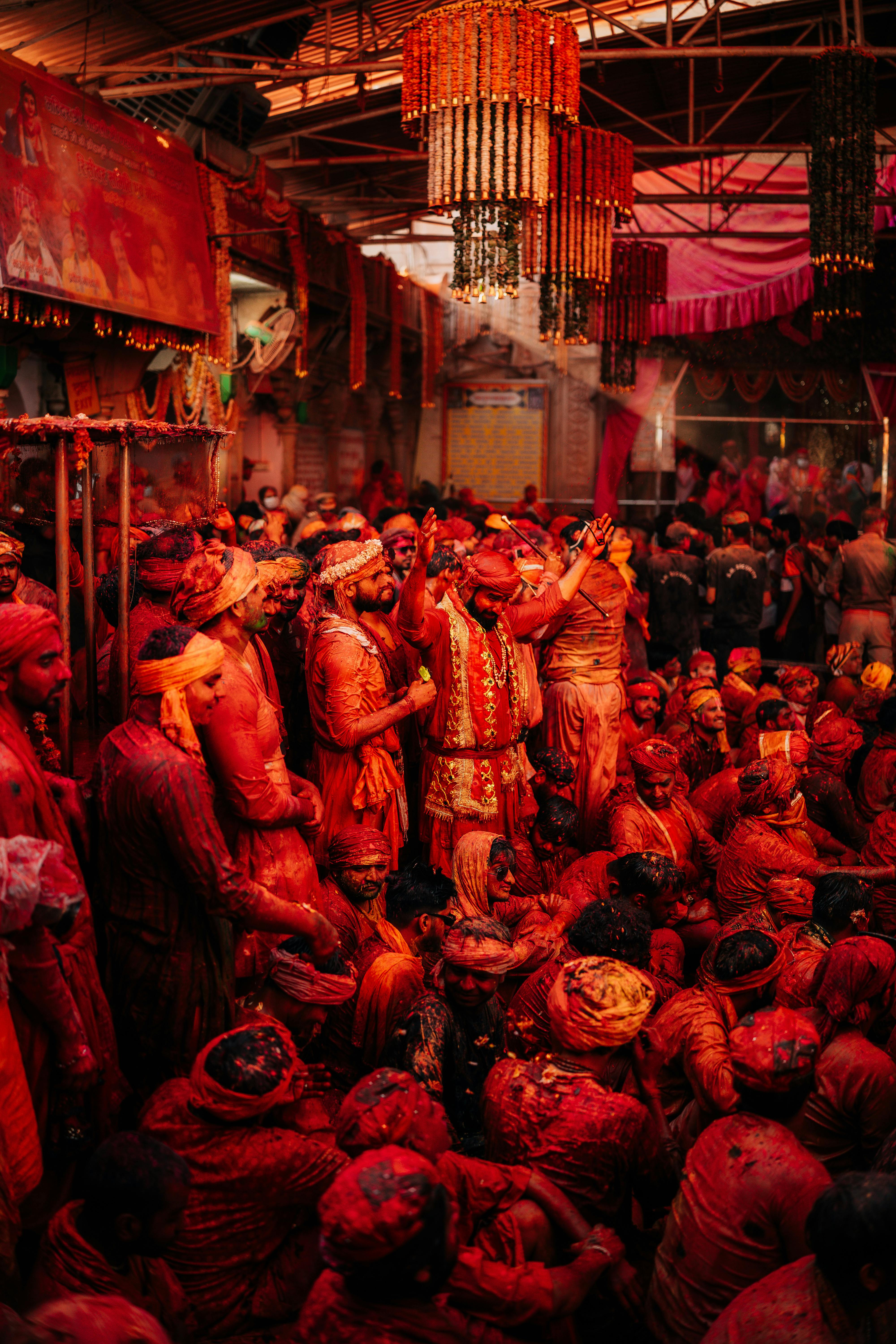 Colorful crowd enjoying Holi festival indoors with vibrant red hues and traditional attire.