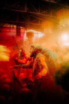 Colorful Holi celebration with people covered in bright powders indoors, capturing festive joy.