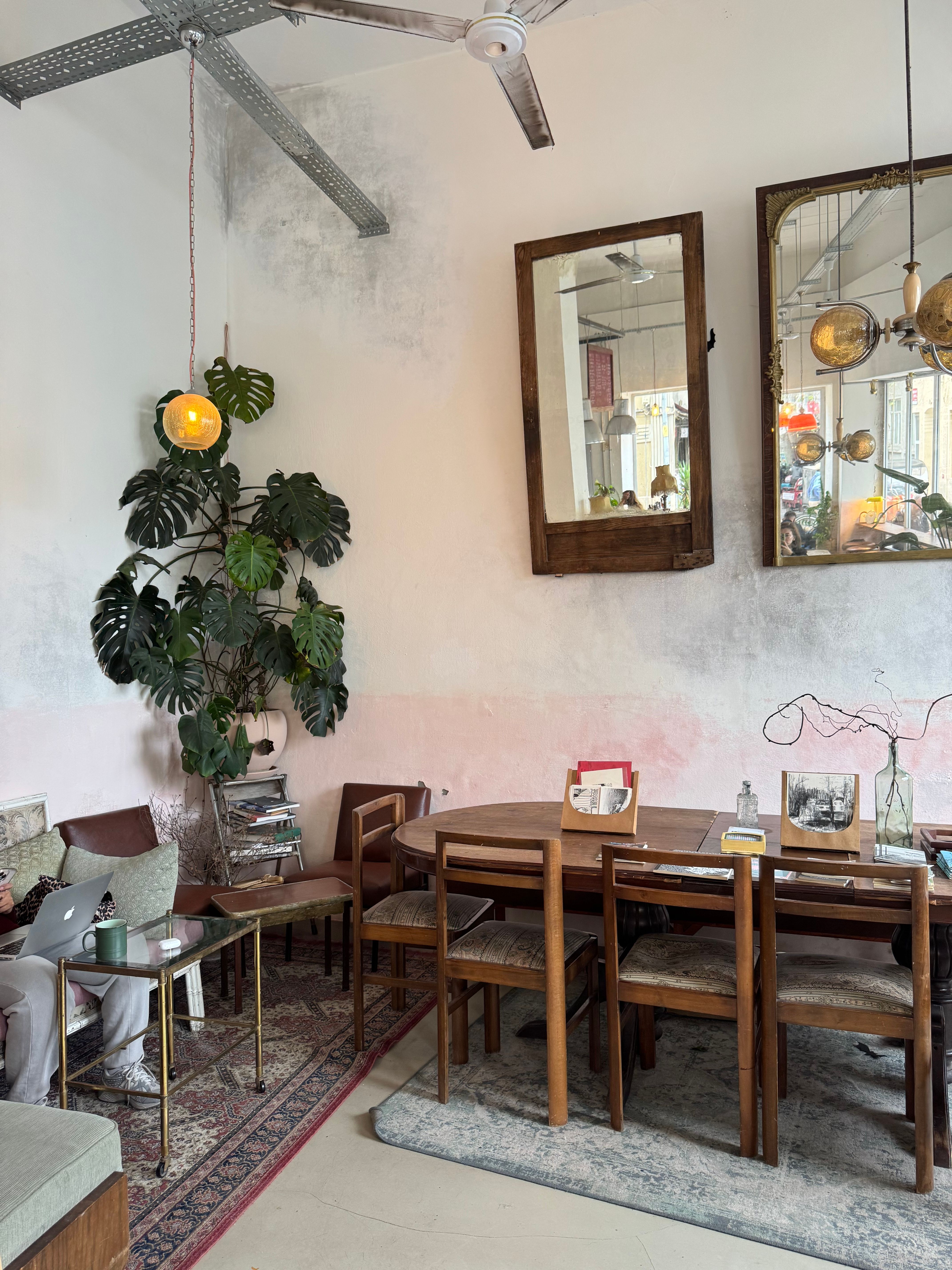 A beautifully designed café interior featuring modern furniture, greenery, and decorative mirrors.