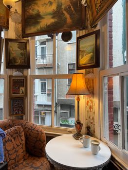 A vintage café corner with framed artwork, a patterned chair, and warm lighting from a table lamp.
