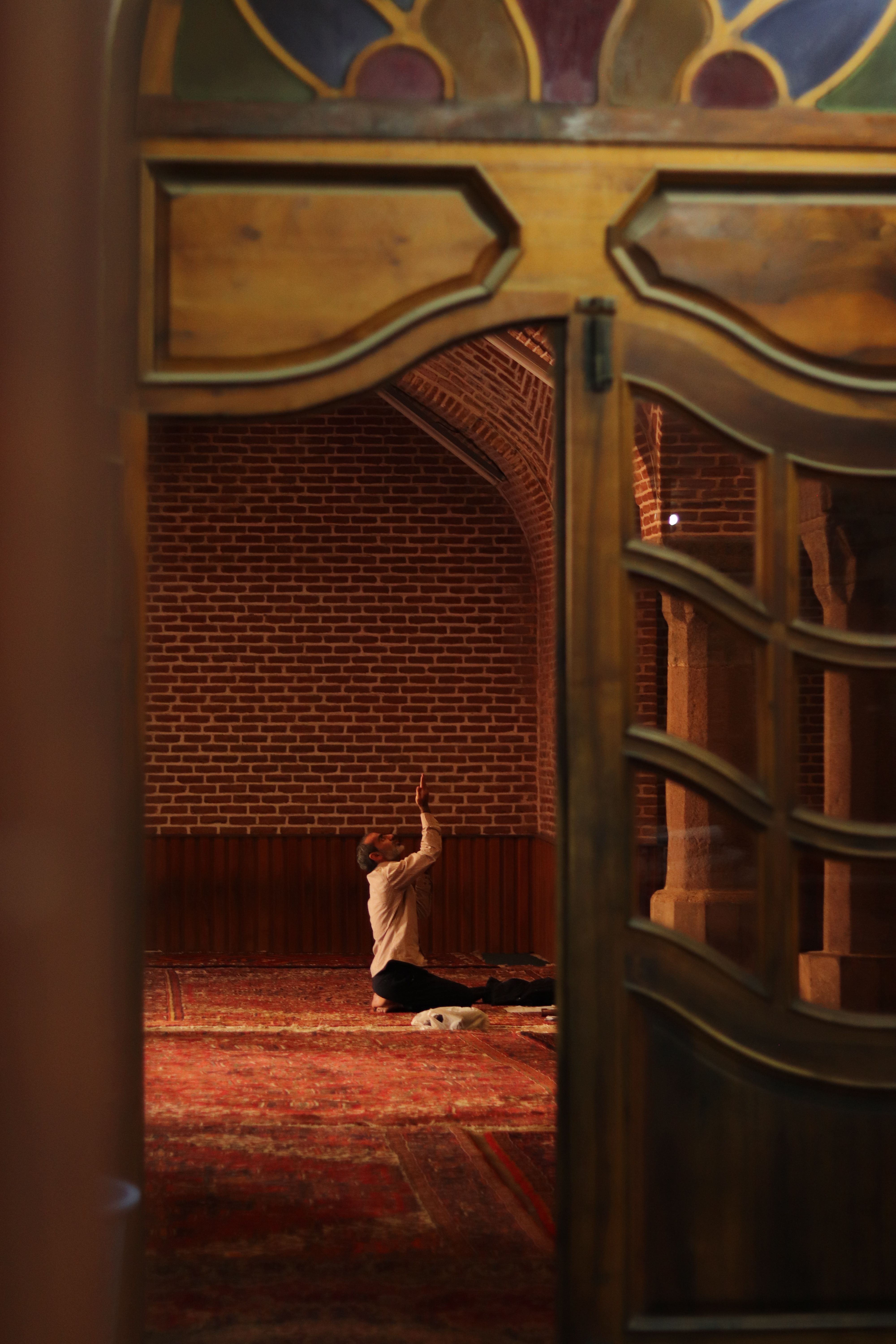A man in prayer inside a historic mosque in Tabriz, showcasing intricate brick arches.
