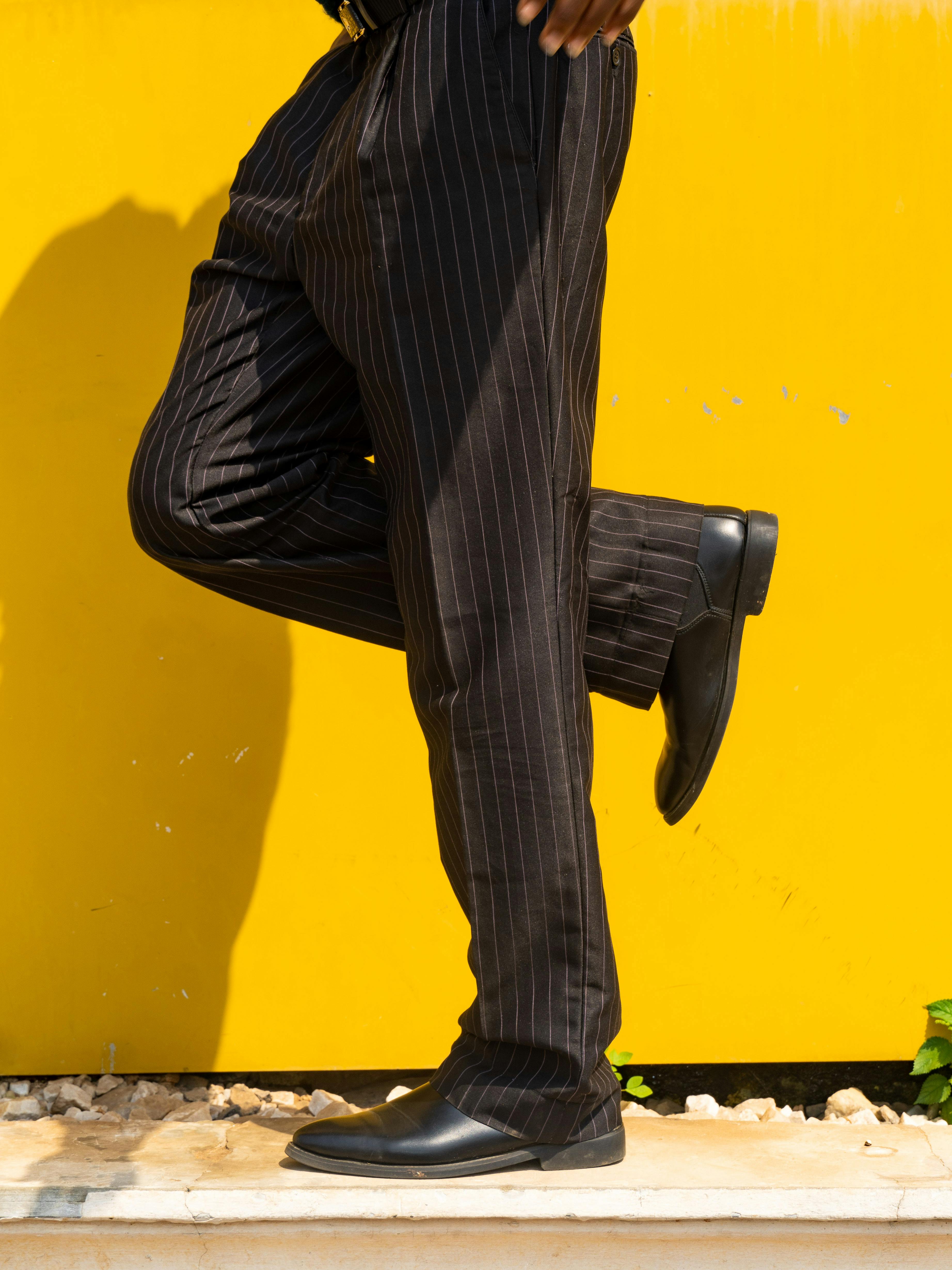 Free Man in pinstripe pants with a yellow backdrop, showing style and motion. Stock Photo