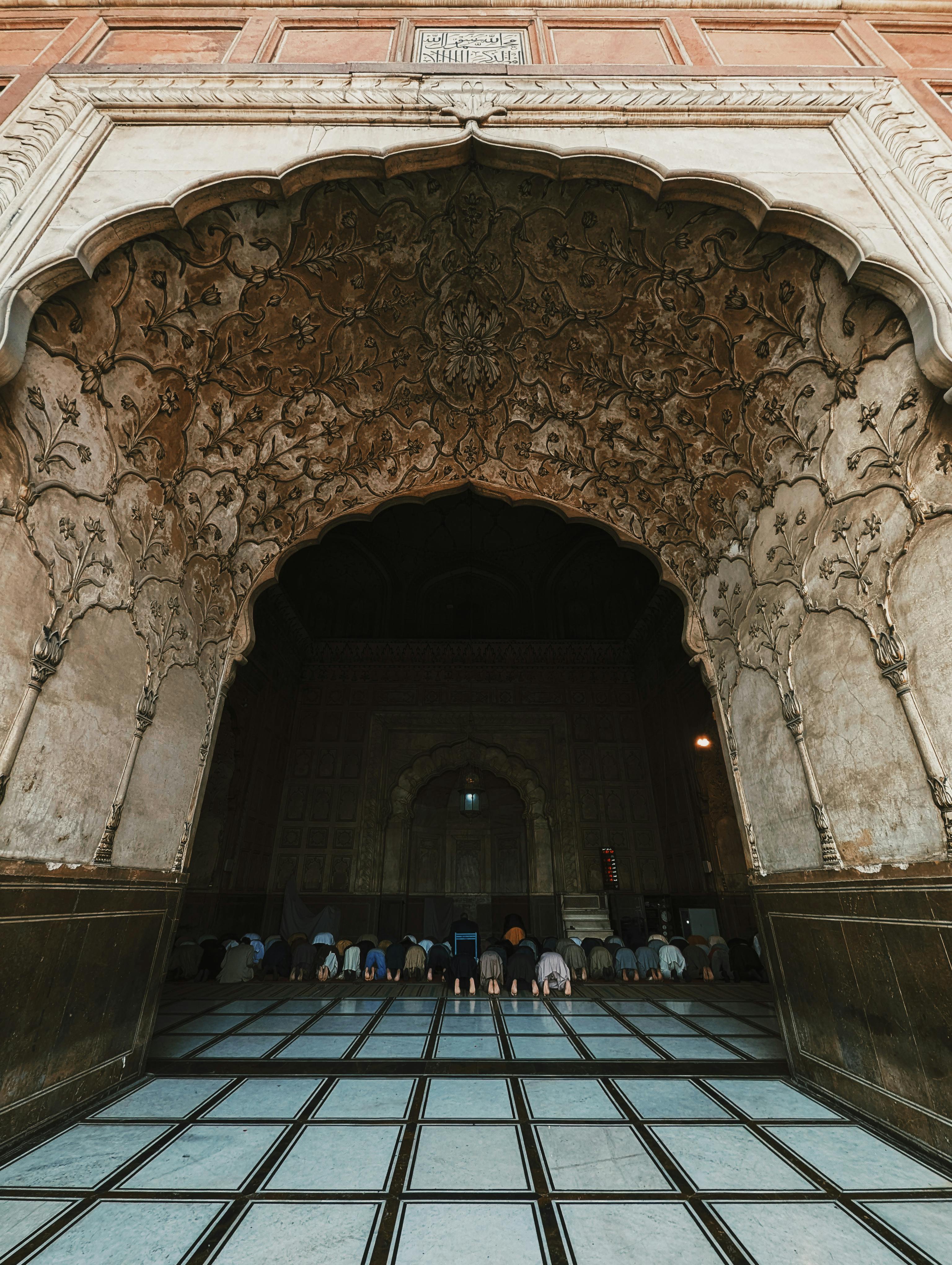 bezplatná Lidé se modlí uvnitř historické mešity s zdobenou klenutou architekturou. Základová fotografie