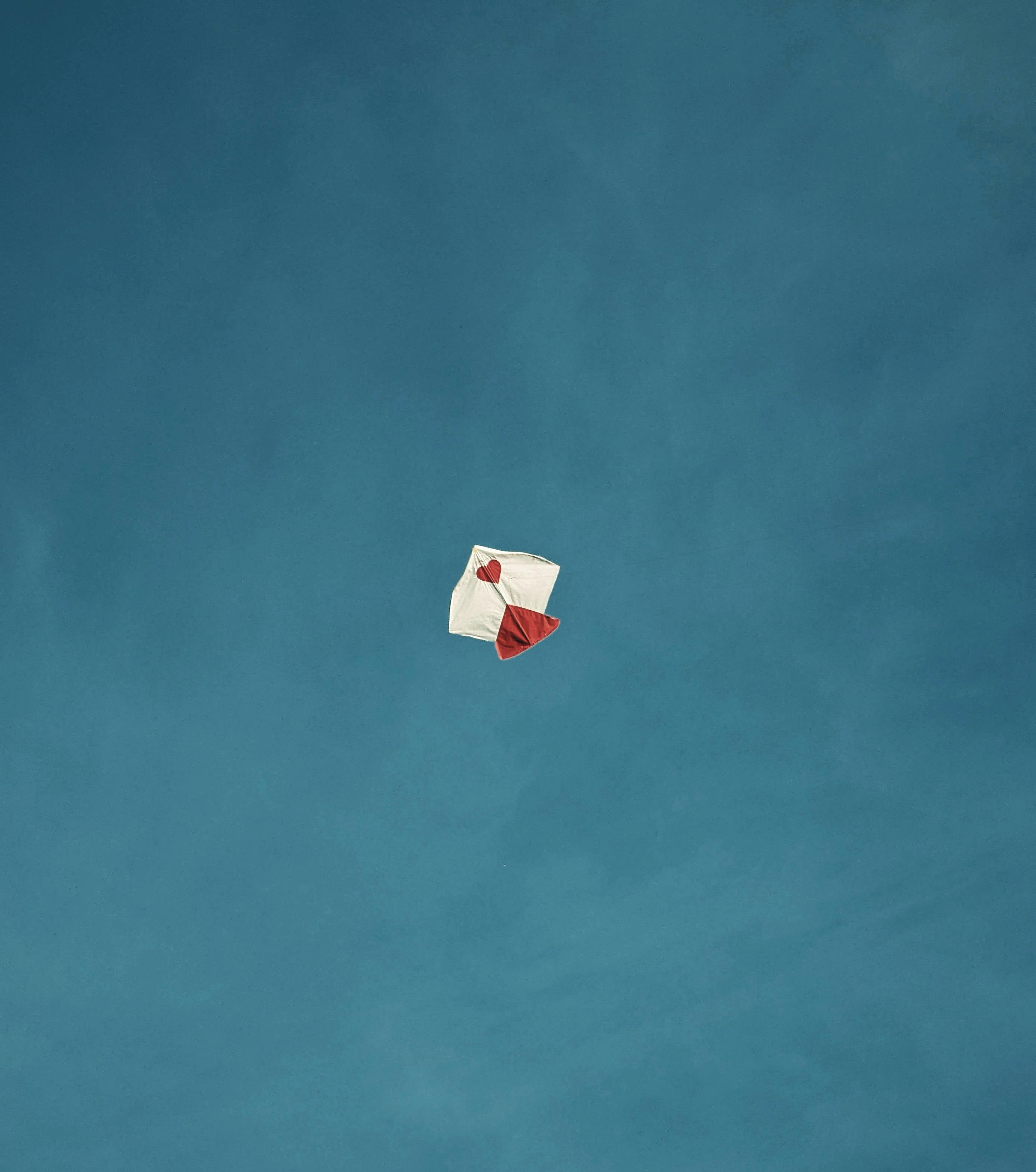 Gratis Una cometa solitaria con tonos rojos y blancos deslizándose con gracia en un cielo azul claro, encarnando la libertad. Foto de stock