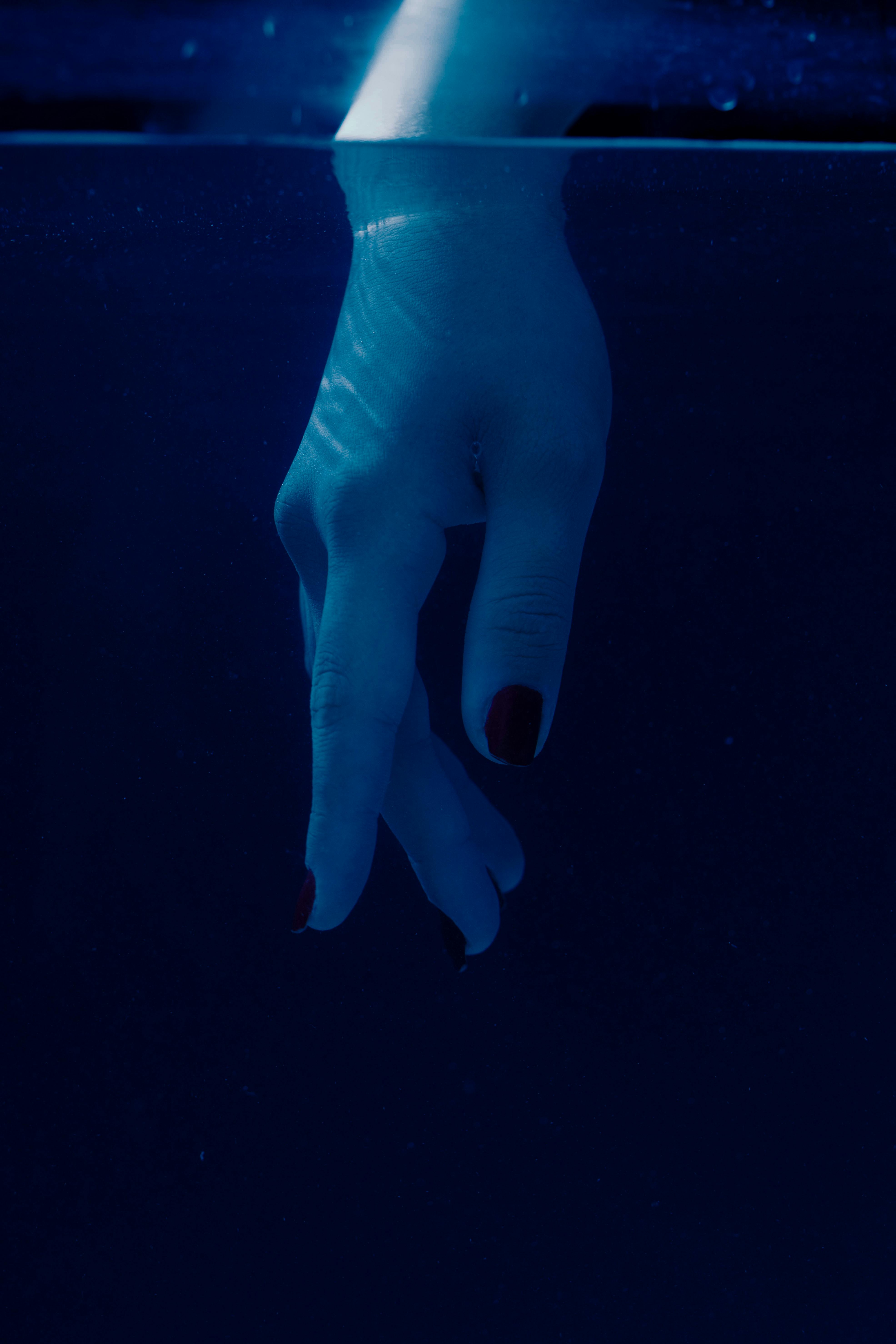 Gratis Una mano con uñas rojas sumergida graciosamente bajo el agua, creando ondas artísticas. Foto de stock