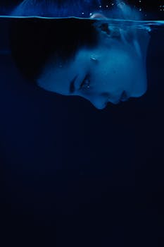 An artistic underwater portrait of a woman in a serene expression, immersed in deep blue water.