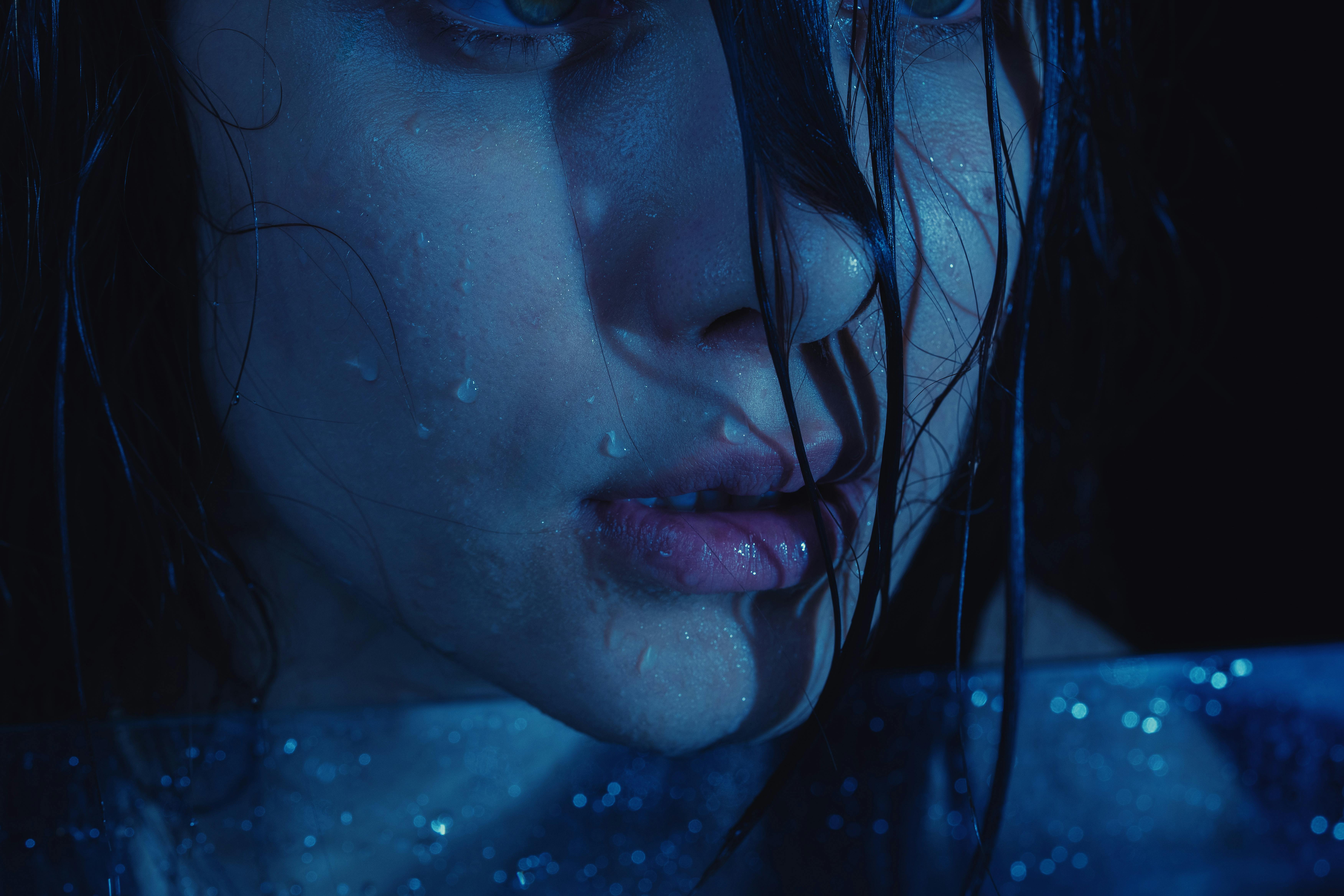 Ilmainen Dramaattinen lähikuva vedessä kastuneesta henkilöstä, jonka sininen valaistus luo tunnelmallisen tunnelman. Kuvapankkikuva