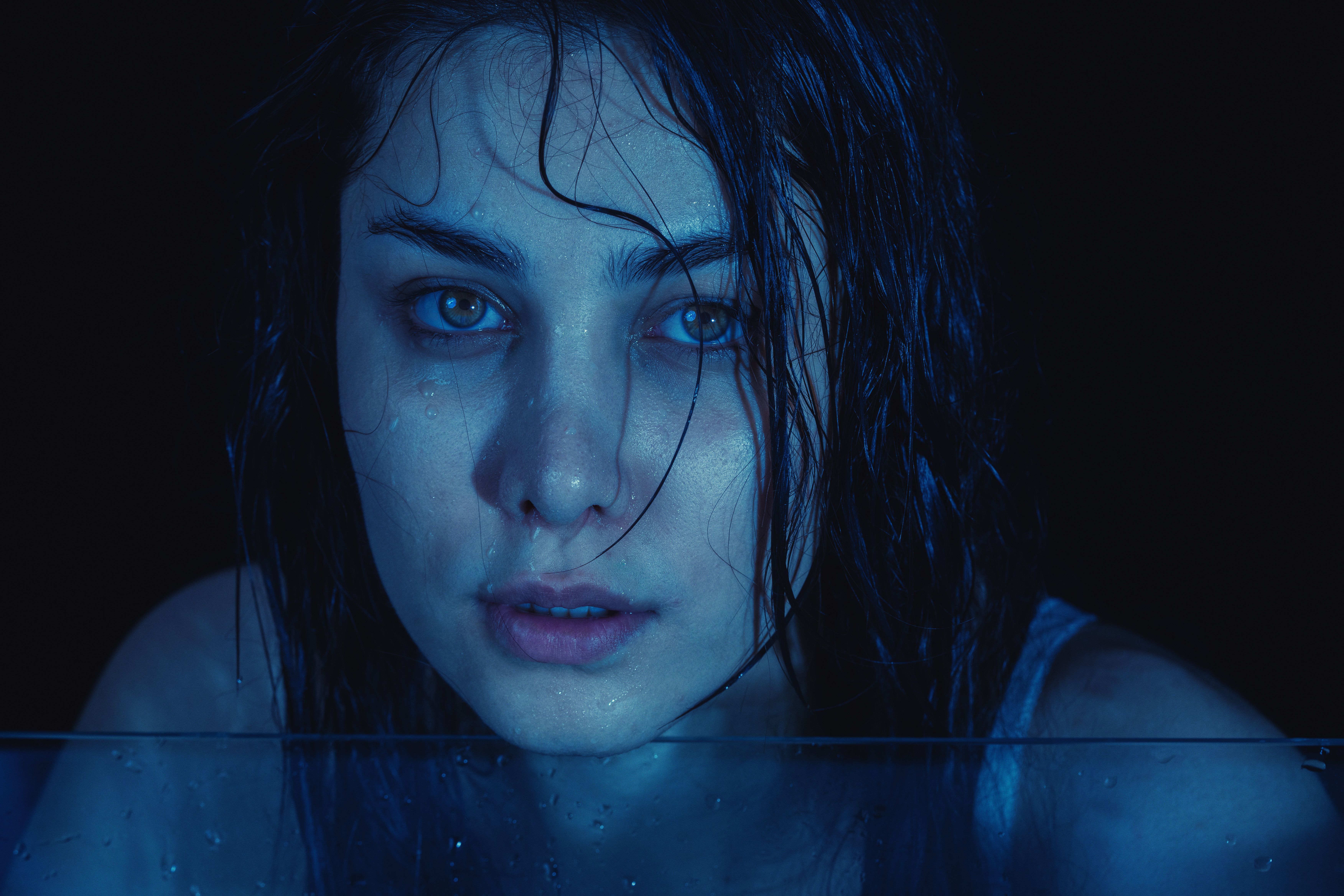 Emotional close-up portrait of a wet woman with a moody, artistic tone under blue lighting.