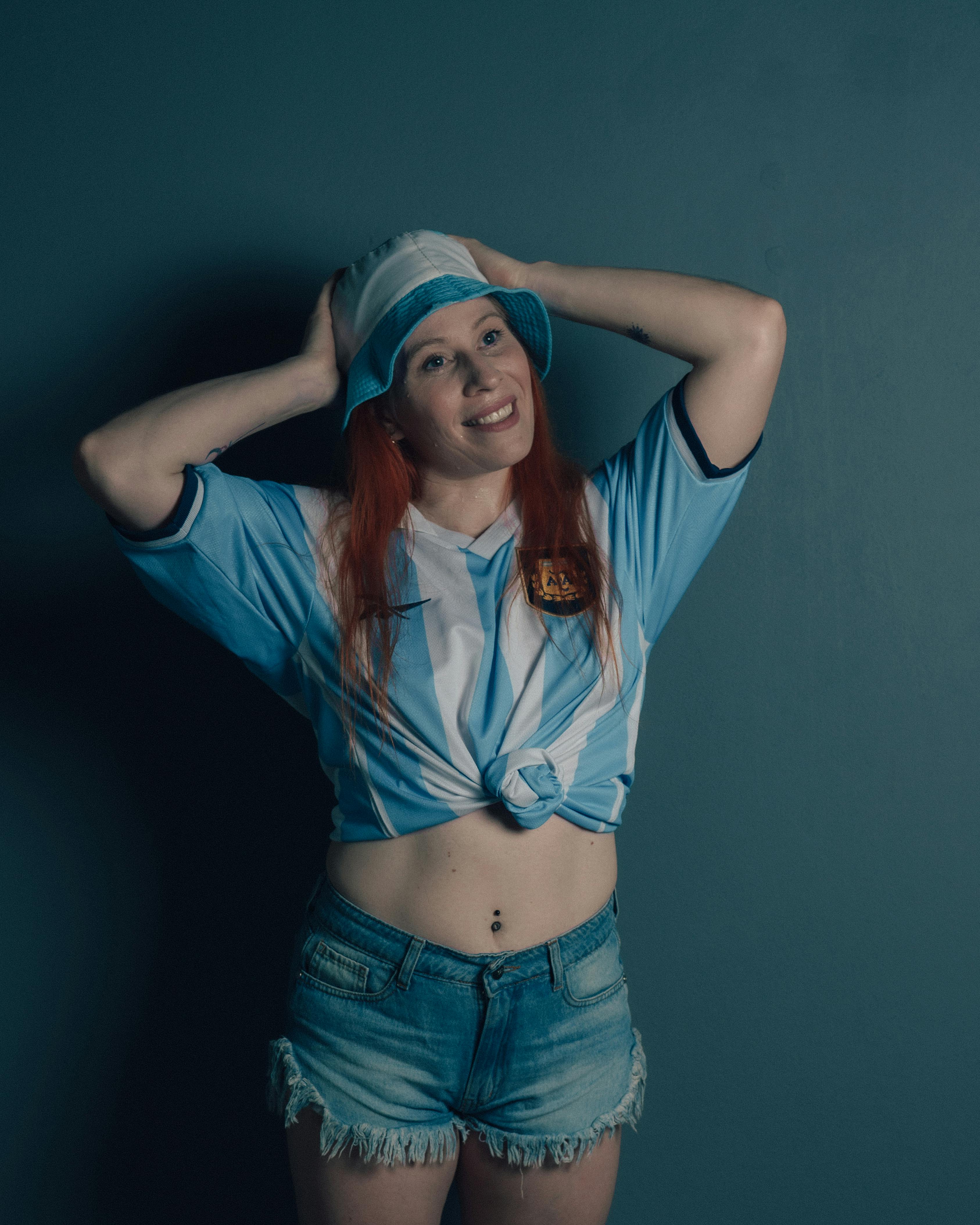 Gratis Una giovane donna sorridente che indossa la maglia della nazionale argentina e un cappello da pescatore si diverte. Foto a disposizione