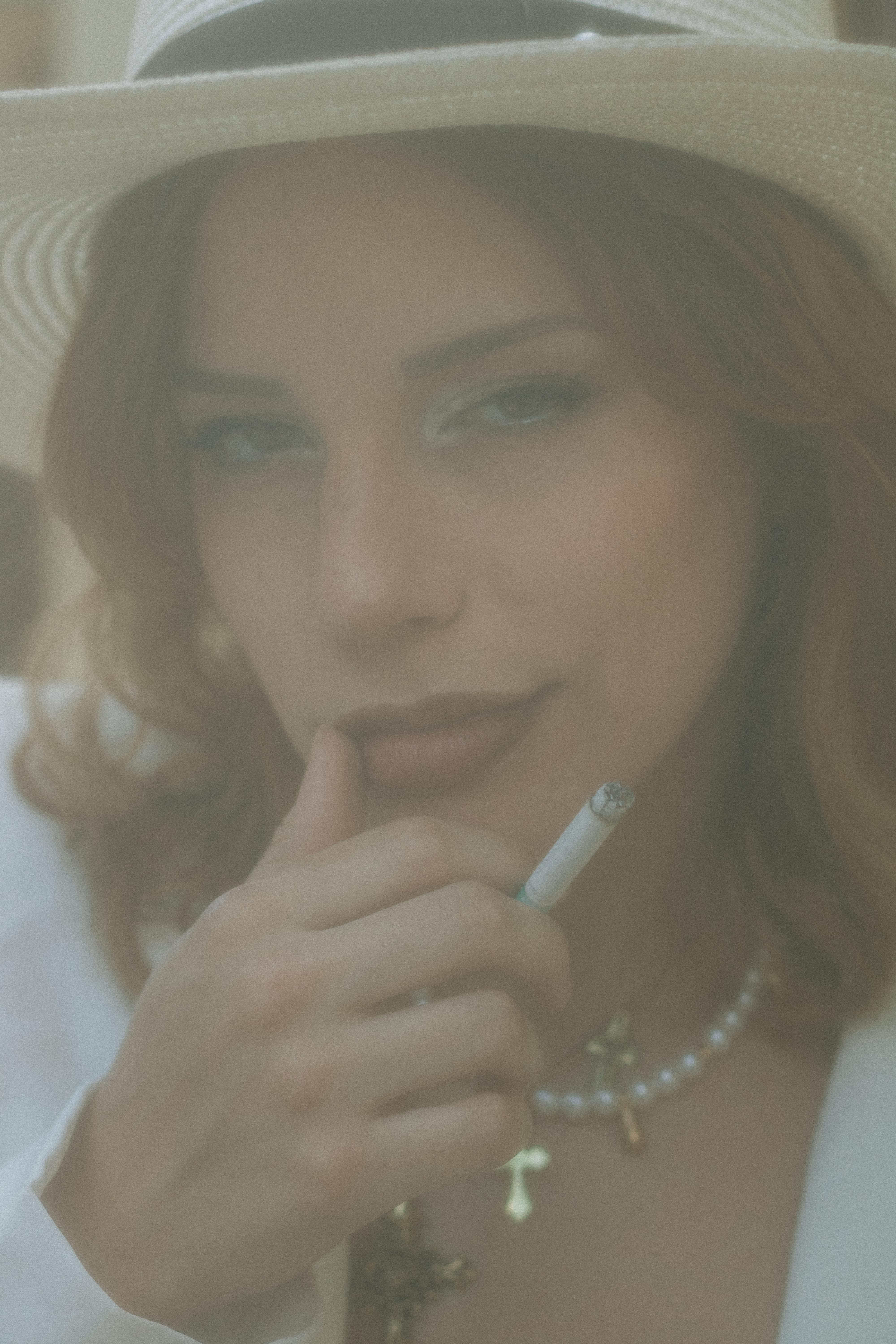 ingyenes Stílusos nő fehér kalapban, cigarettával a kezében, vintage hangulatot árasztva. Stockfotó