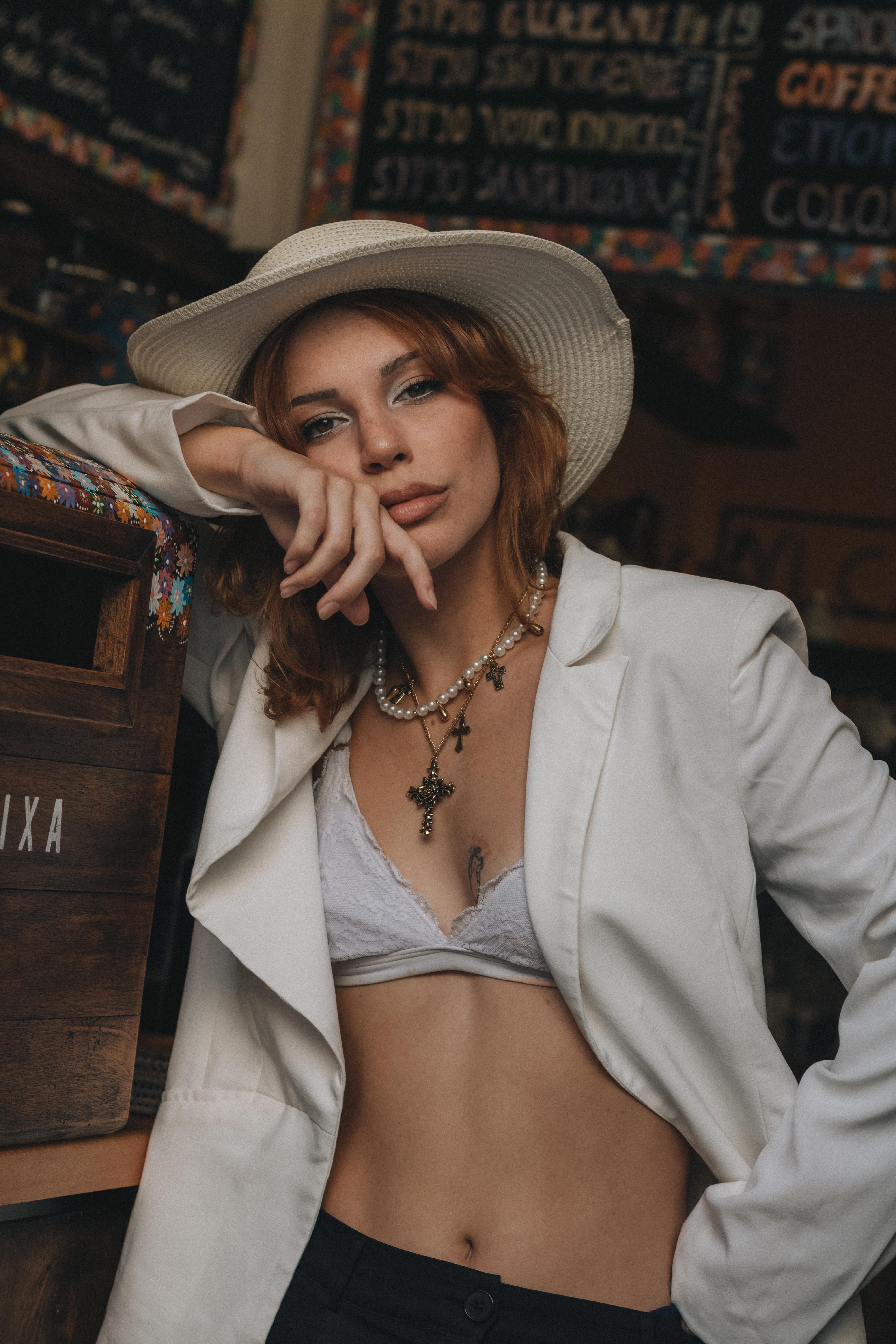 bezplatná Módní žena pózující v kavárně s bílým kloboukem a sakem, vyzařující sebevědomí a styl. Základová fotografie