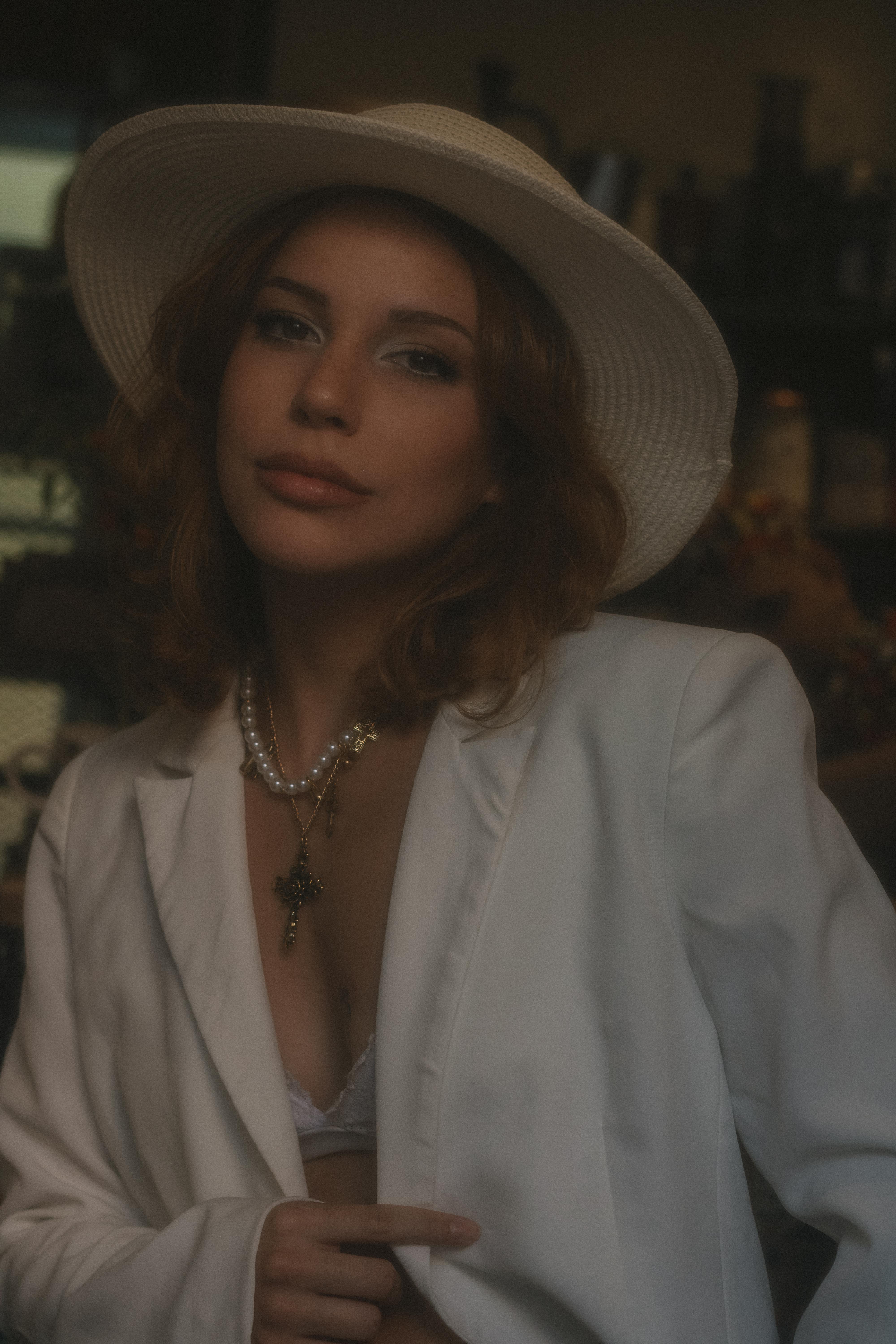 Безкоштовне Стильна жінка у білому костюмі та капелюсі елегантно позувала в приміщенні, створюючи вишуканий настрій. стокове фото