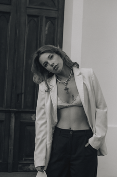 Stylish woman in white blazer and jewelry posing confidently outdoors.