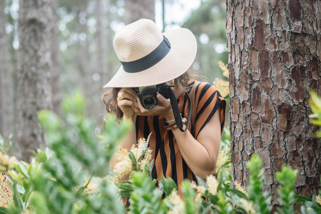 Woman in White Hat and Black and Yellow Stripe Tank Top Standing Beside Brown Tree during Day