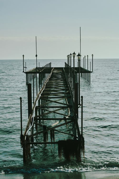 Free A weathered pier stretches into the ocean under a serene sunset sky, evoking tranquility. Stock Photo
