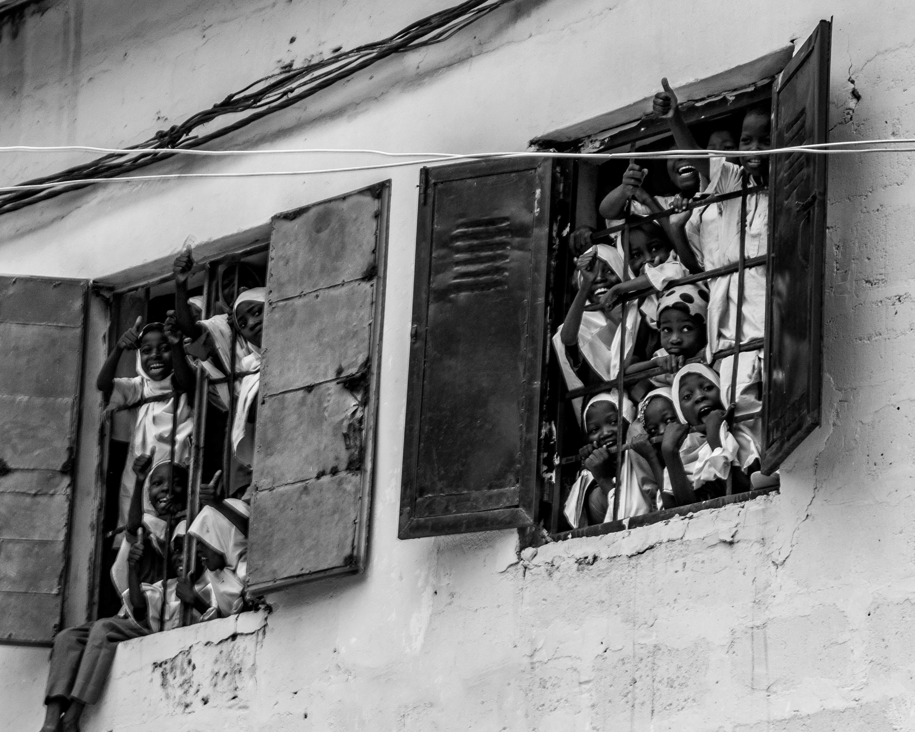 De franc Grup de nens somrient i saludant des de les finestres d'un edifici antic, capturats en blanc i negre. Foto d'estoc