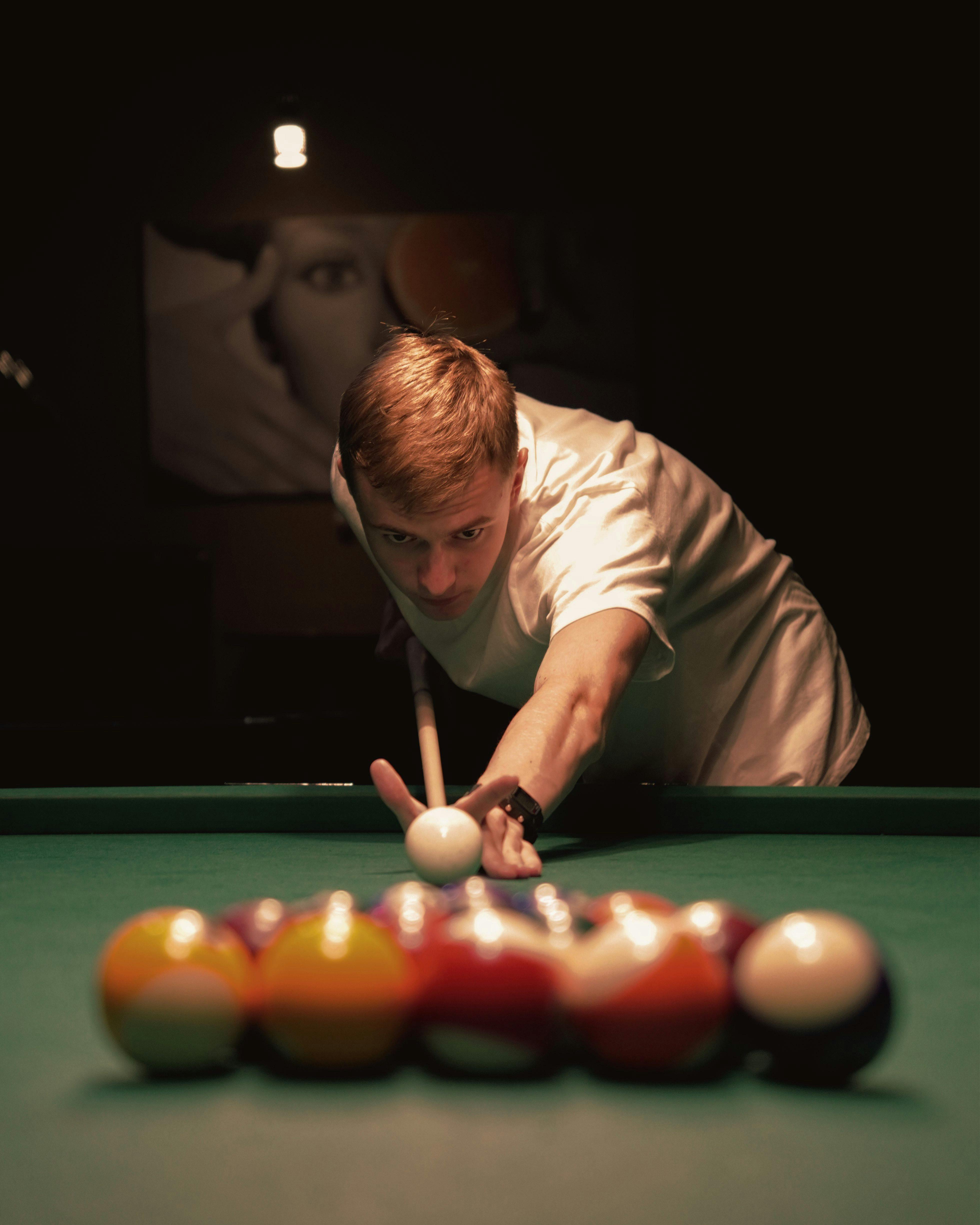 Free A young man intensely focuses on making a billiard shot in a dimly lit room. Stock Photo