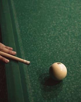 Detailed view of a billiard setup with cue stick and ball ready for strike on green table.