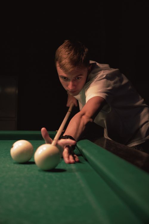 Free A young man intensely focuses on making a pool shot, with a dimly lit billiard table in an indoor setting. Stock Photo
