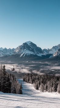 Snow-capped mountain and ski lift with forest in winter, creating a serene natural scene.
