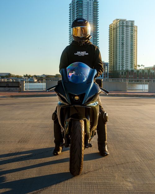 Free A motorcyclist in gear faces the camera on an urban bridge with city skyline. Stock Photo
