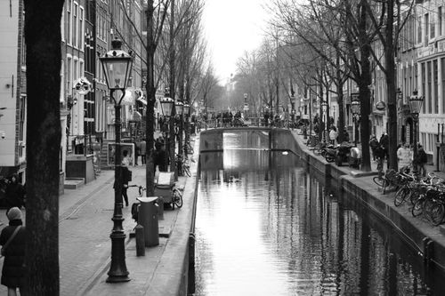 Free A captivating black and white view of Amsterdam's iconic canal reflecting its historic architecture and lively streets. Stock Photo