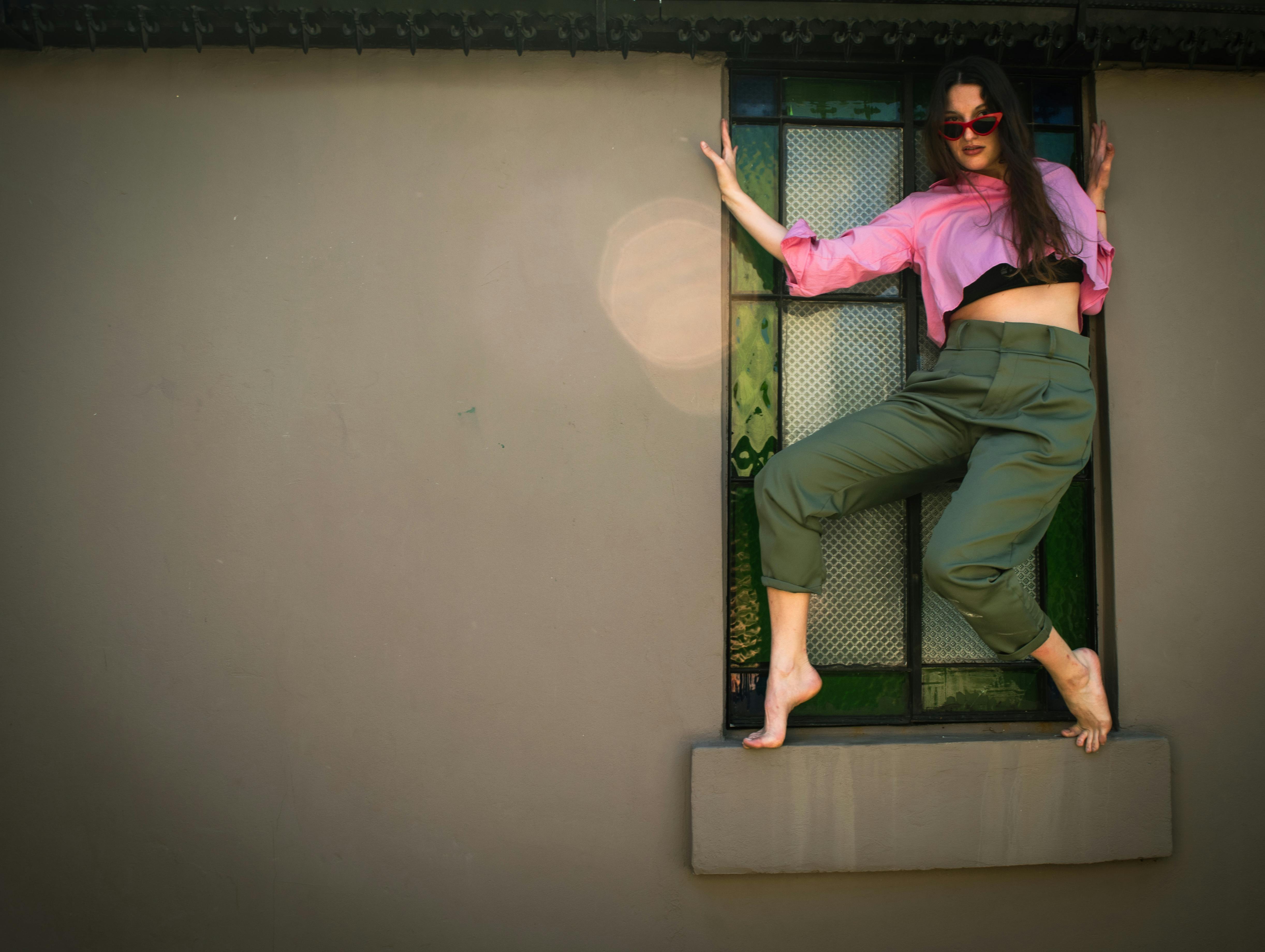 Gratis Una donna in abiti colorati posa in modo creativo vicino a una vetrata, mettendo in risalto moda ed espressione. Foto a disposizione