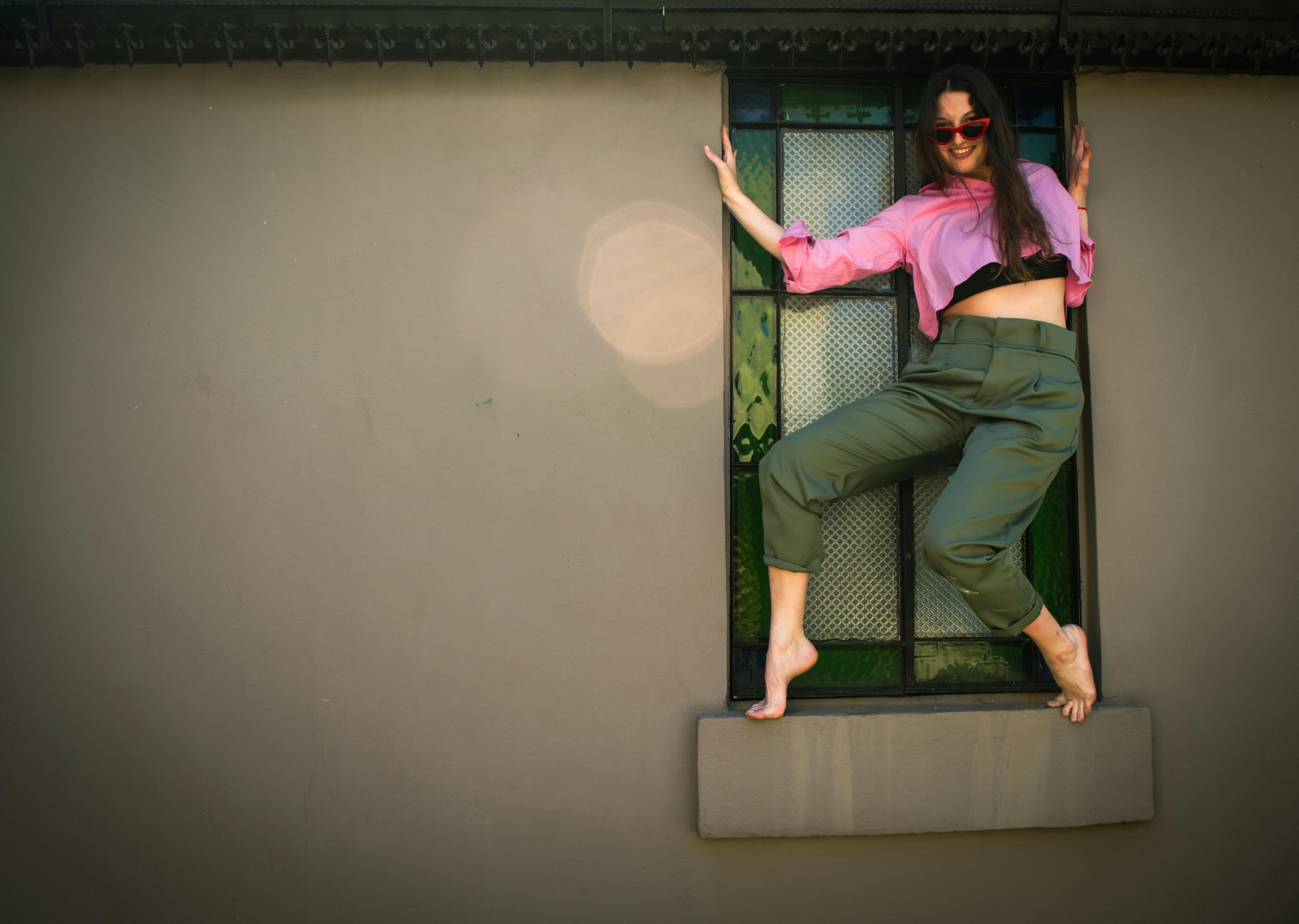 Miễn phí Một cô gái trẻ trong bộ quần áo rực rỡ đang nô đùa trèo lên khung cửa sổ vào một ngày nắng đẹp. Ảnh lưu trữ