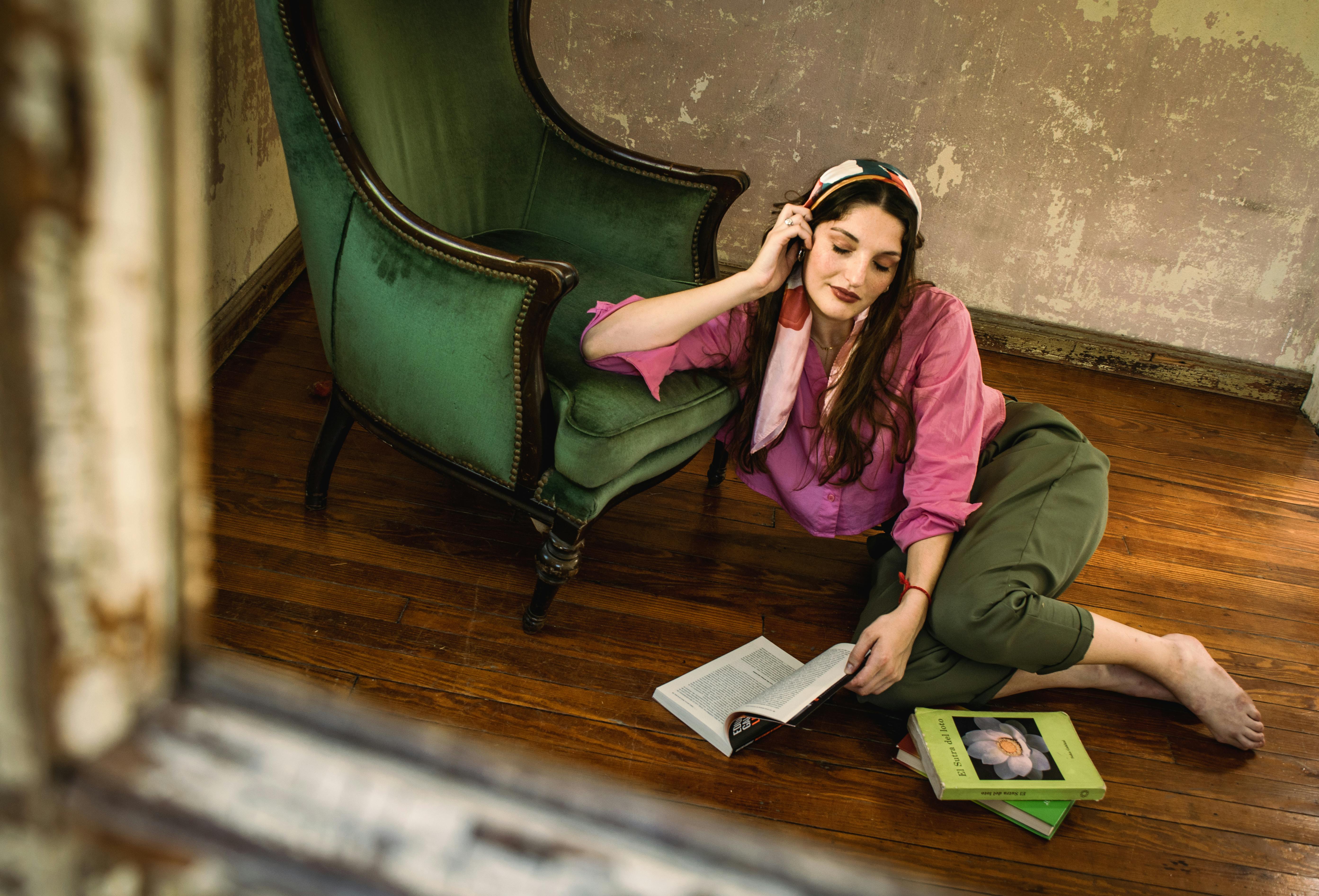 ฟรี หญิงสาวกำลังพักผ่อนอ่านหนังสือบนพื้นข้างเก้าอี้สีเขียวในห้องสไตล์ชนบท คลังภาพถ่าย