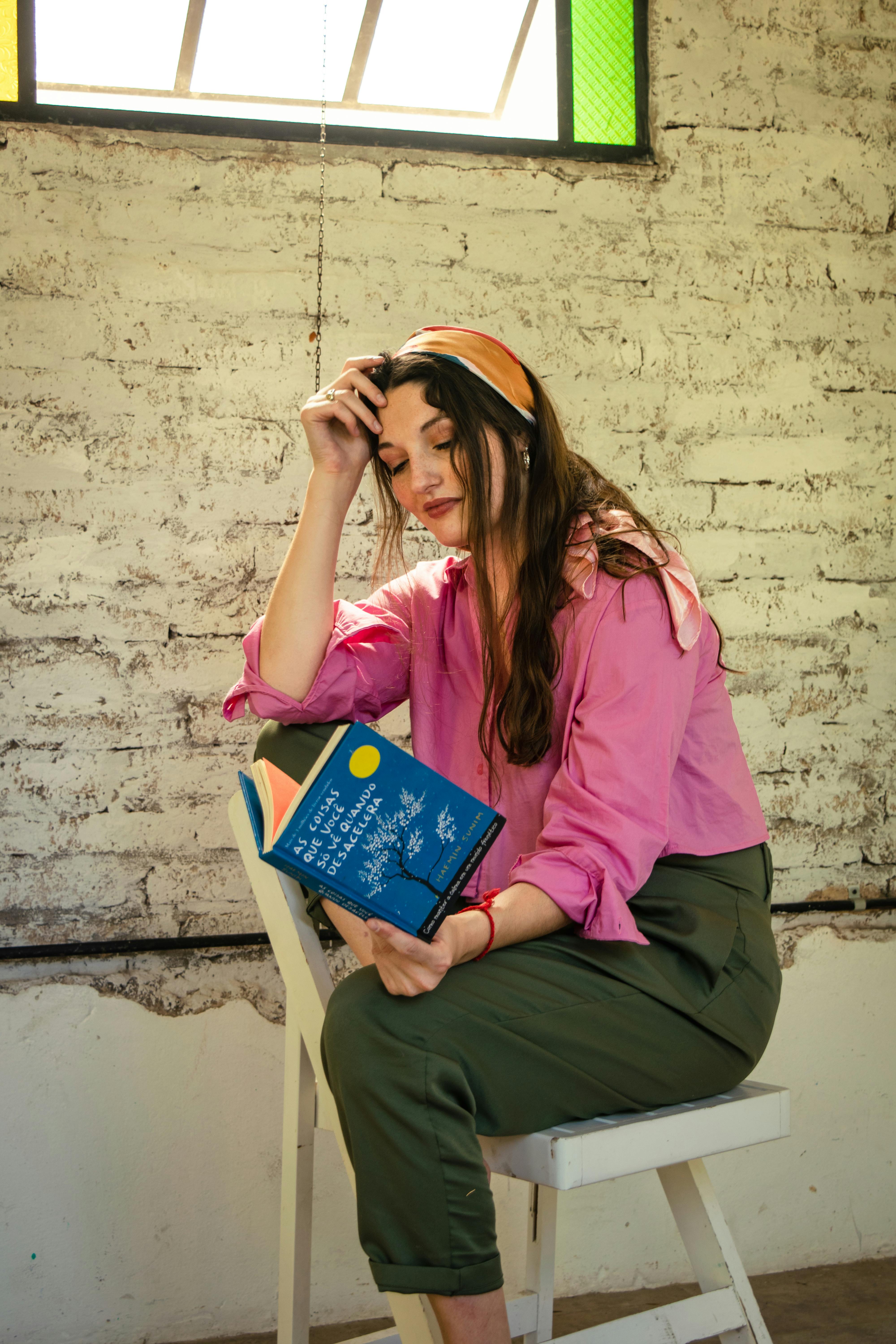 Miễn phí Một cô gái trẻ mặc áo sơ mi hồng đang đọc sách bên cửa sổ, tận hưởng khoảnh khắc thư giãn trong nhà. Ảnh lưu trữ