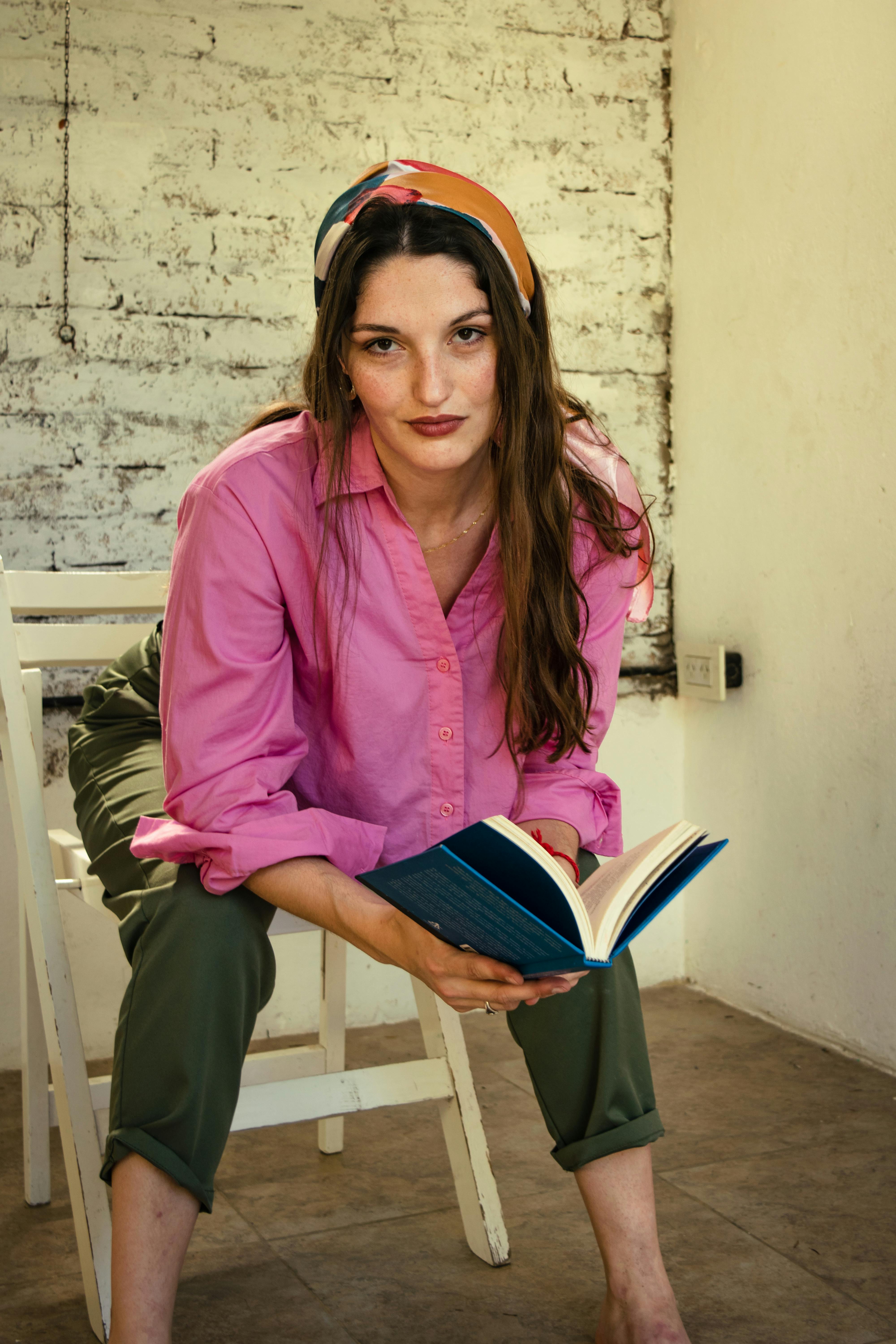 Ilmainen Rento muotokuva naisesta vaaleanpunaisessa paidassa lukemassa kirjaa sisätiloissa. Kuvapankkikuva