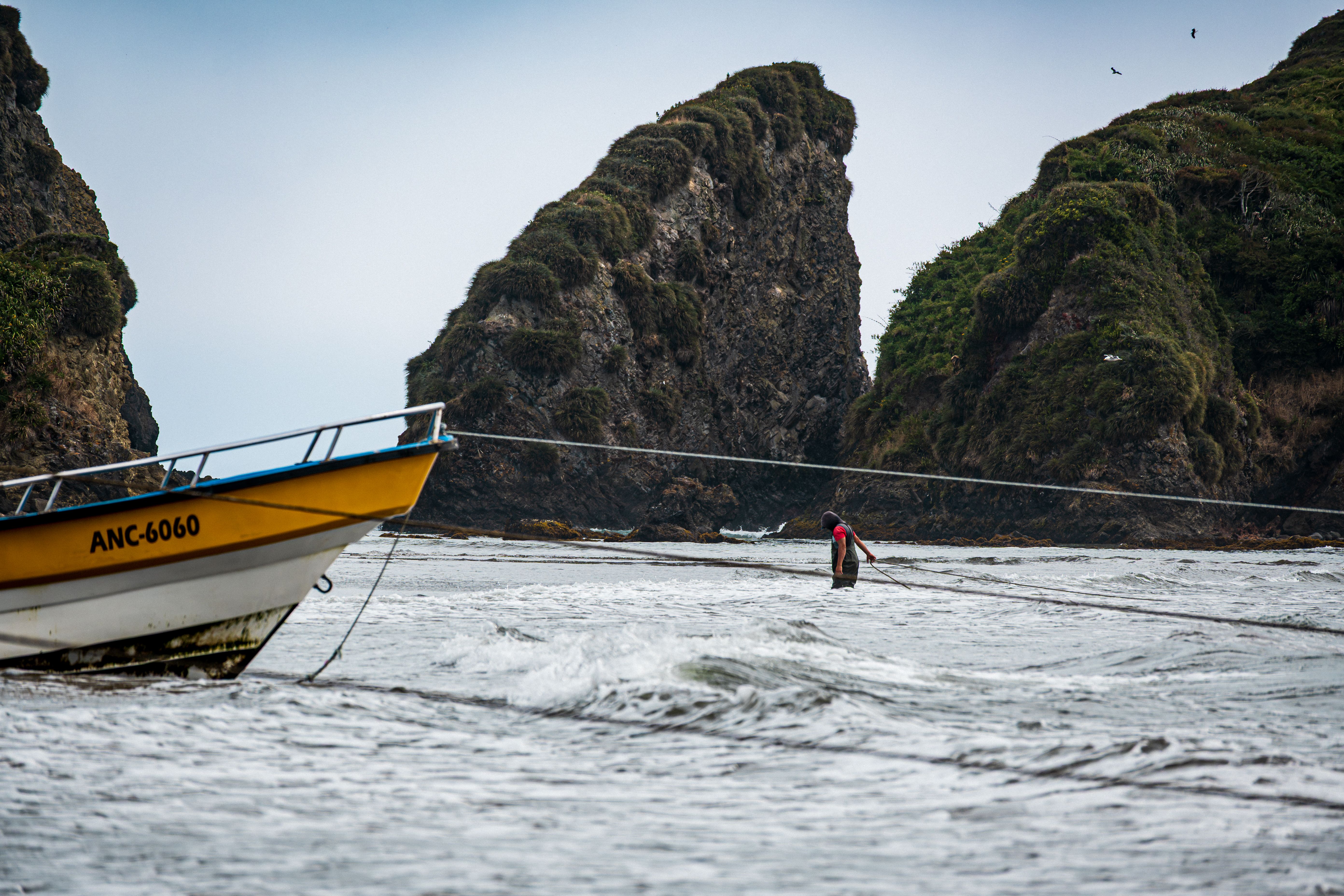 Fotomural Un barco pesquero y un pescador cerca de acantilados rocosos en un día costero en Ancud, Chile.
