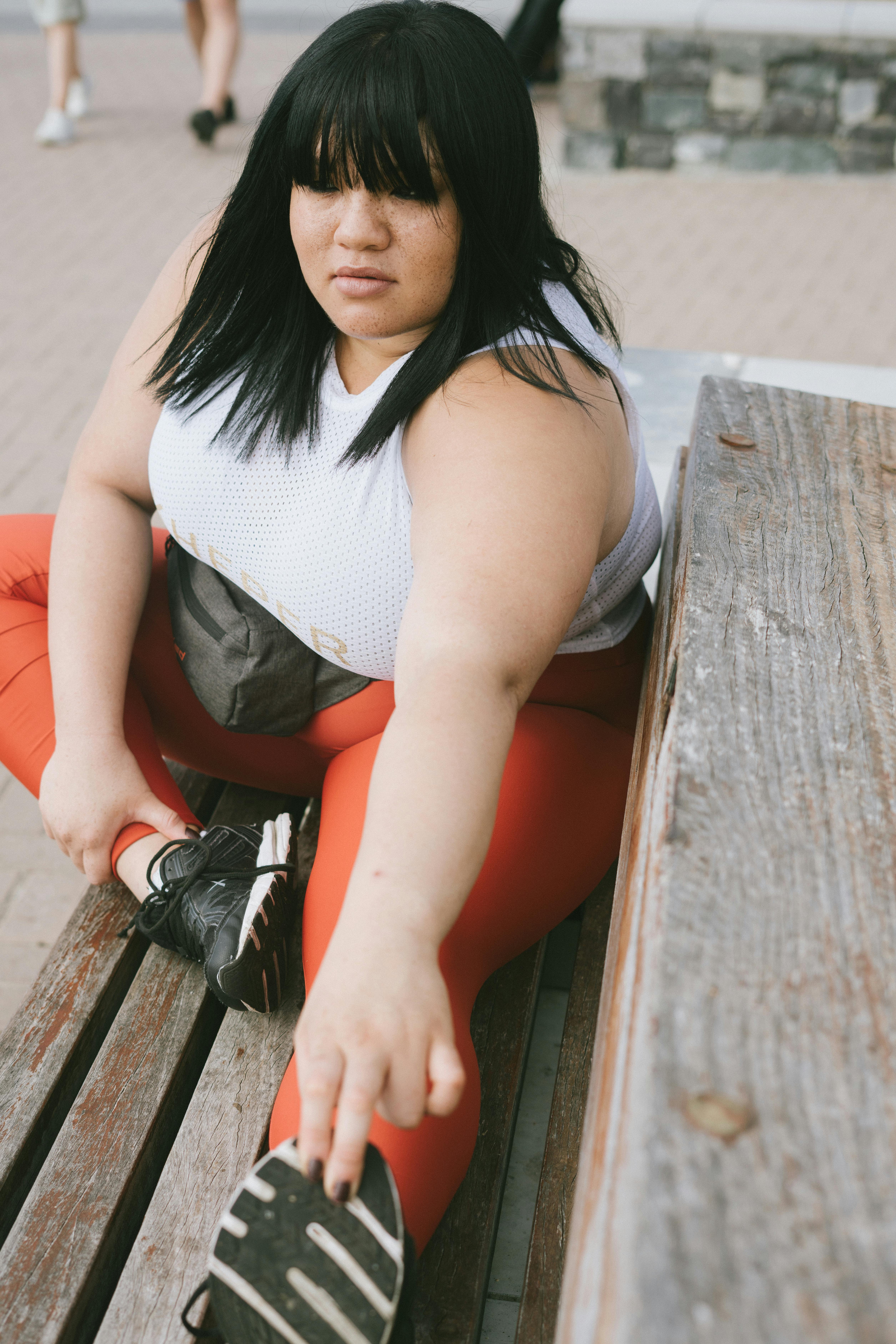 woman in white tank top and red leggings sitting on brown wooden bench