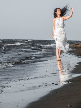 A serene scene of a woman in a white dress walking on a sandy beach with ocean waves.
