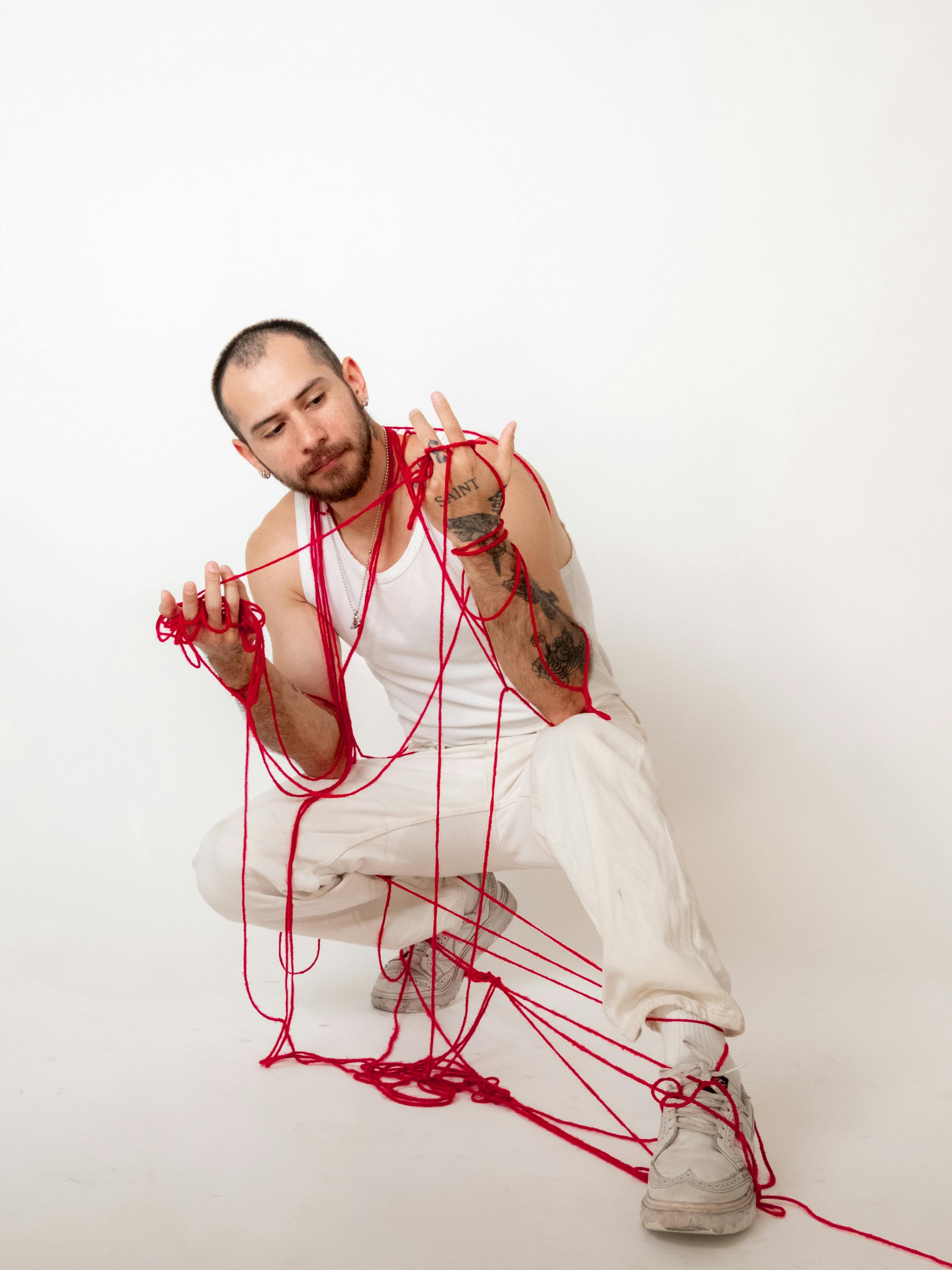 Miễn phí Người đàn ông tạo dáng nghệ thuật với sợi len đỏ trên nền trắng, thể hiện sự sáng tạo và phong cách. Ảnh lưu trữ