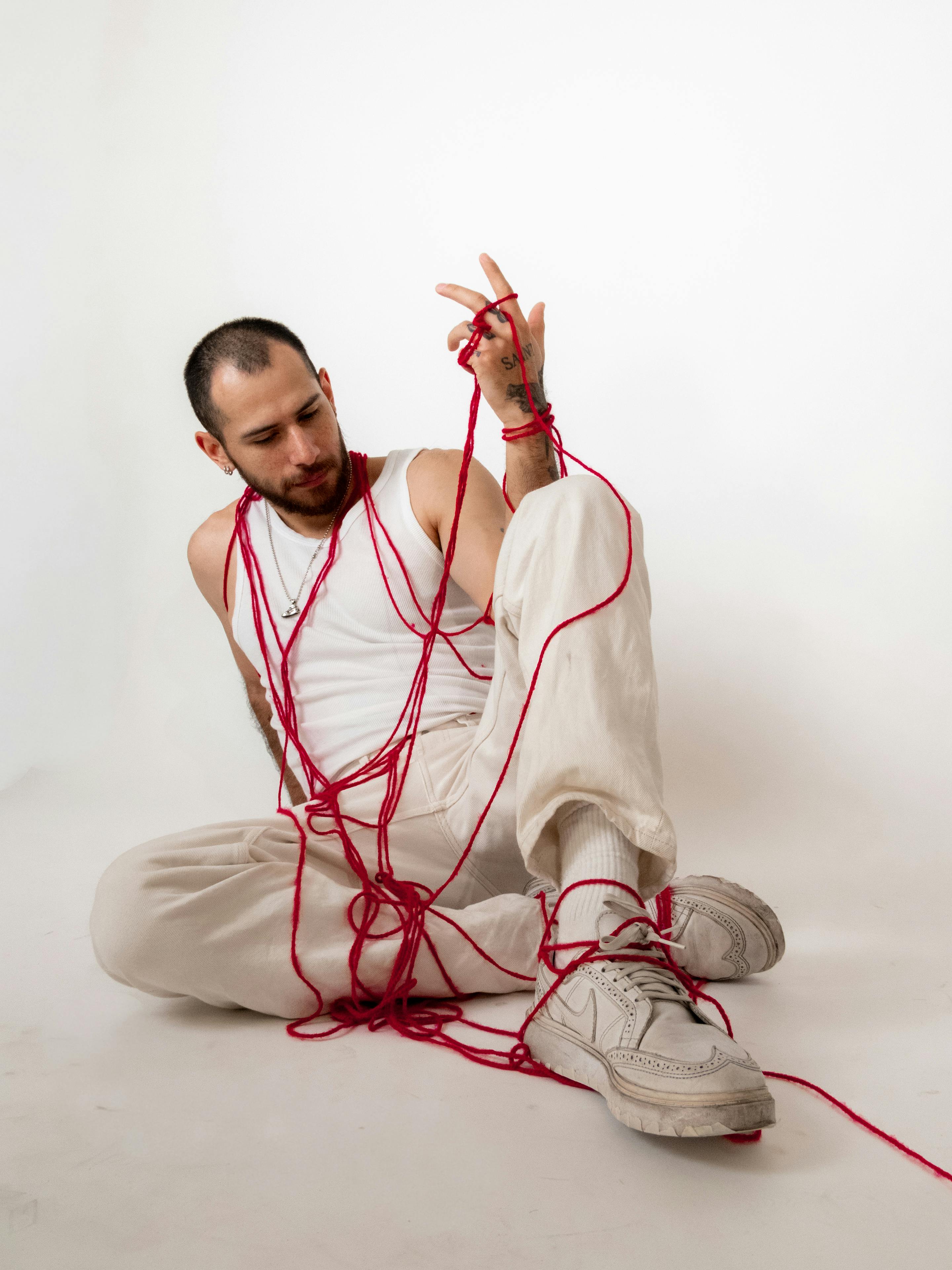 Free A man entangled in red thread posing in a studio environment with a minimalistic white backdrop. Stock Photo