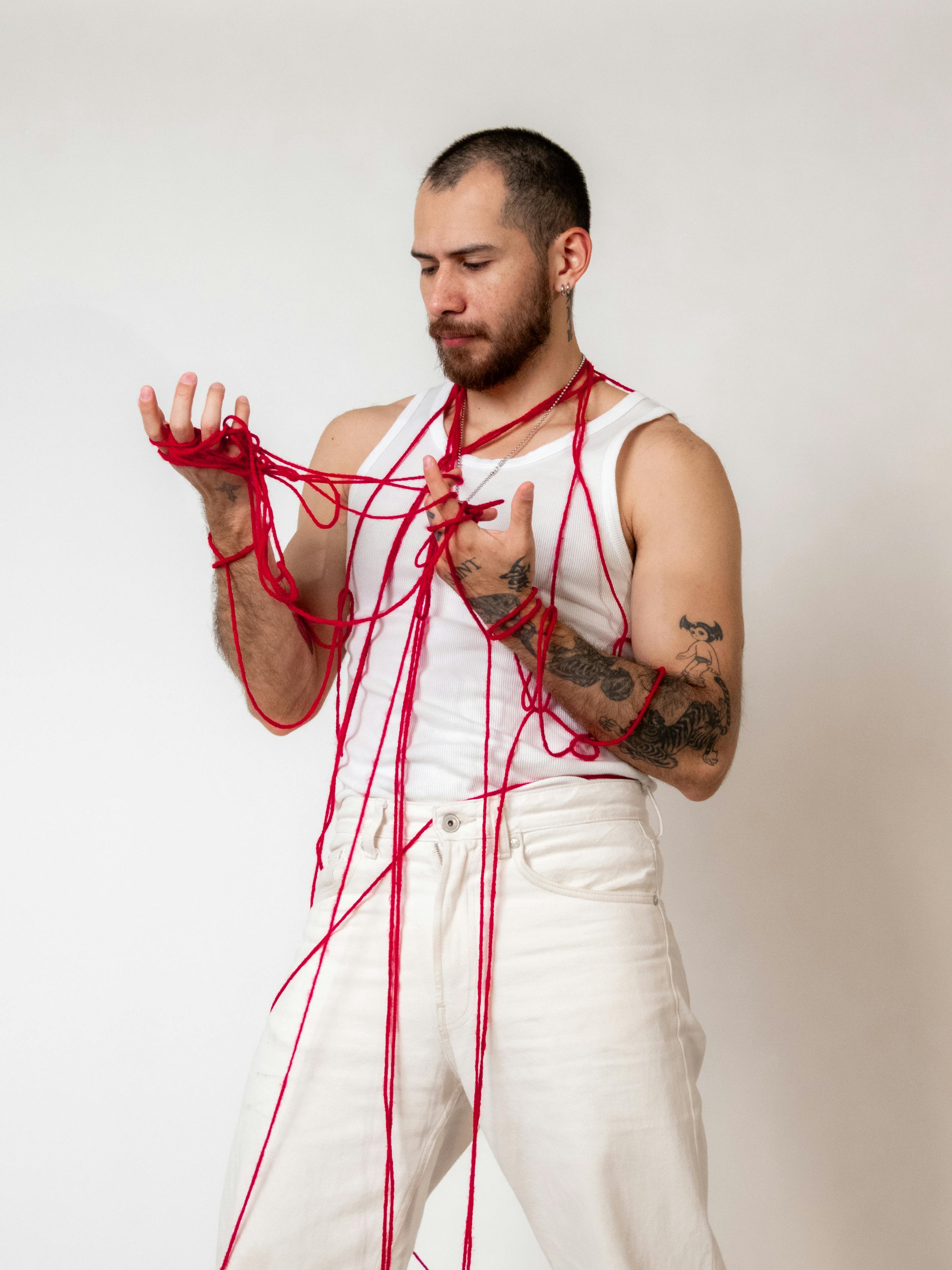 Gratis Un uomo posa avvolto in un filo rosso in una foto creativa scattata in uno studio fotografico. Foto a disposizione