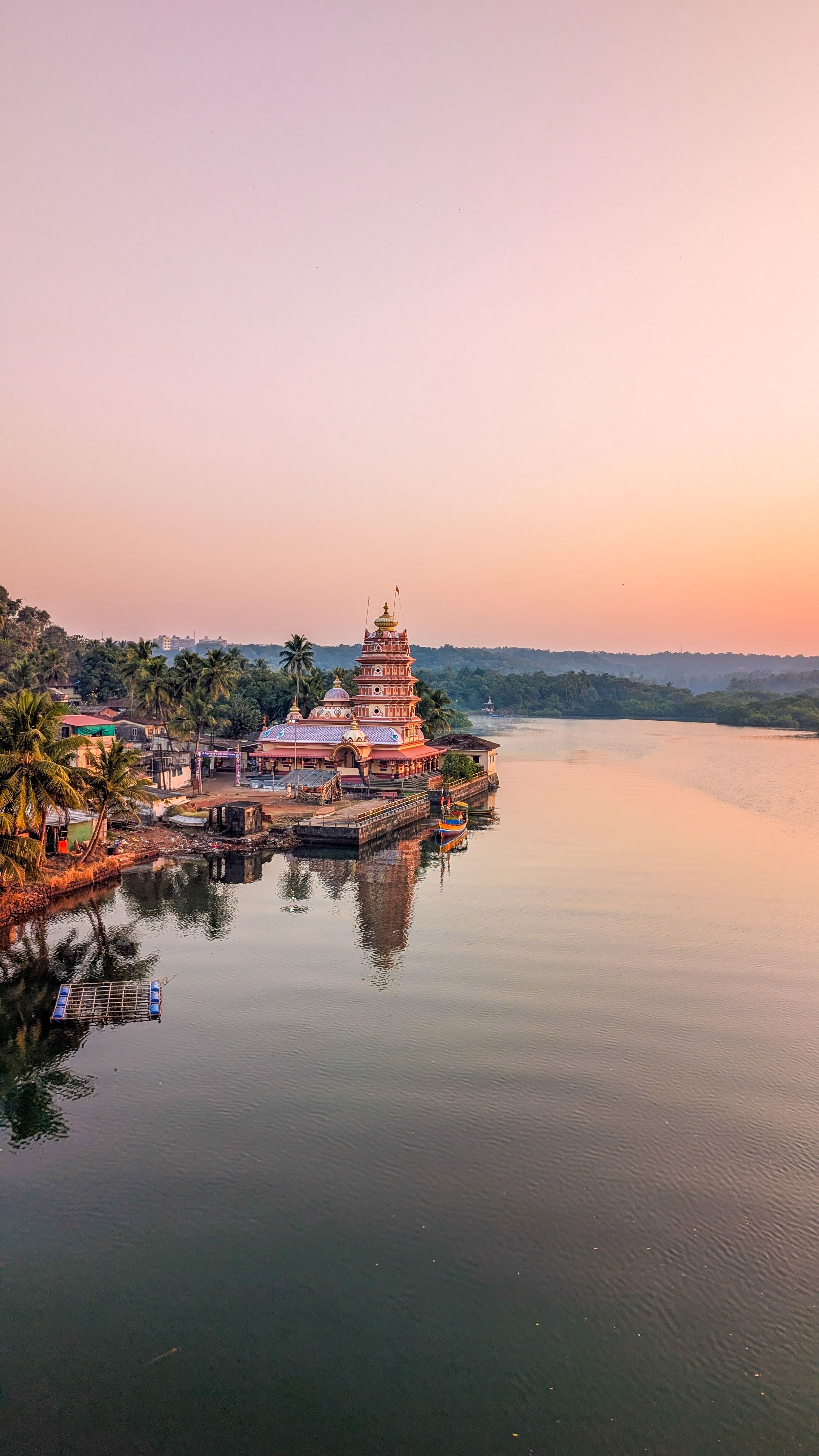 A beautiful temple by the river reflects in the calm water during a stunning sunset.