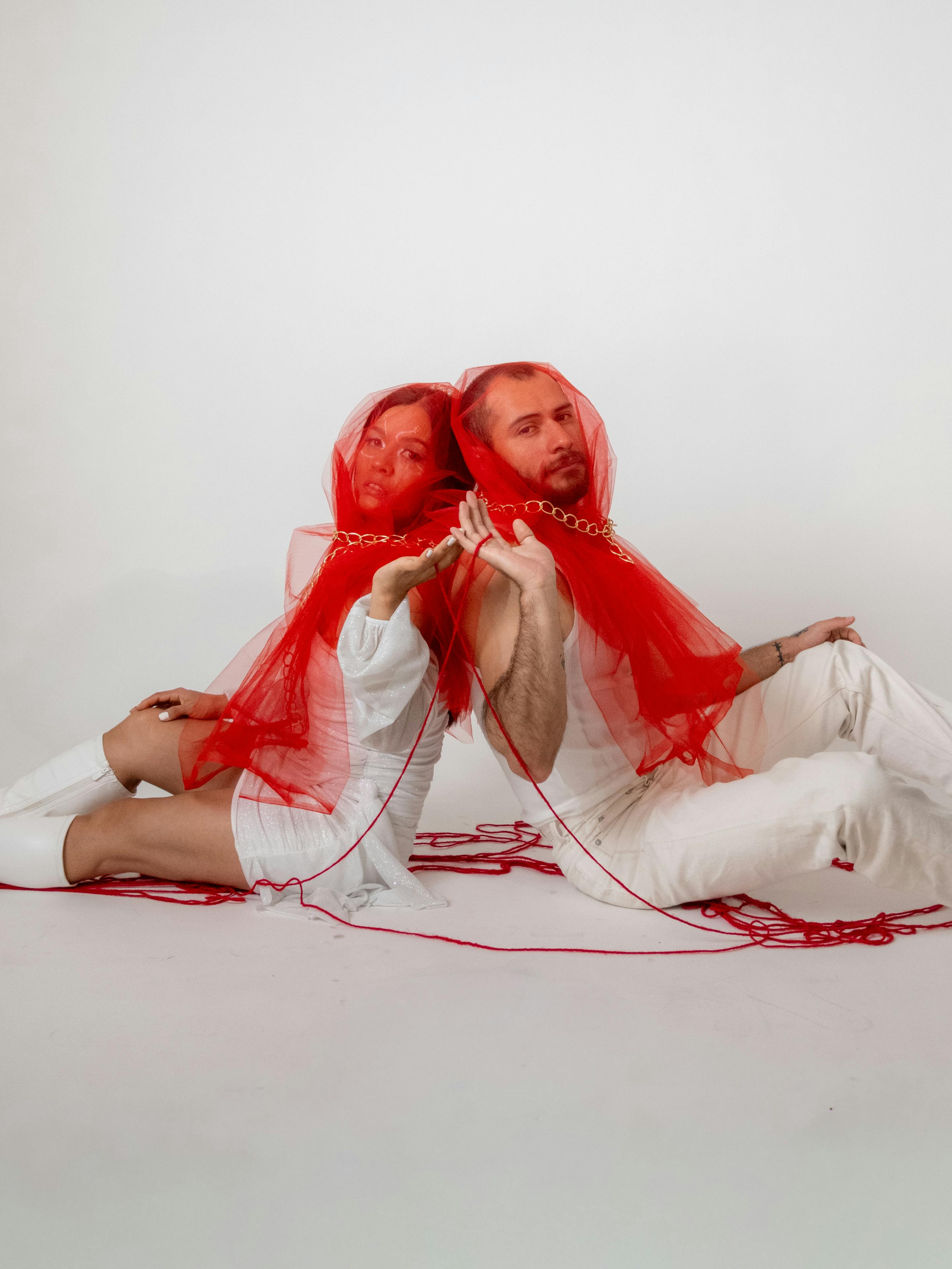 Free Artistic portrait of a couple with red veils in a studio setting, showcasing modern fashion and creative expression. Stock Photo